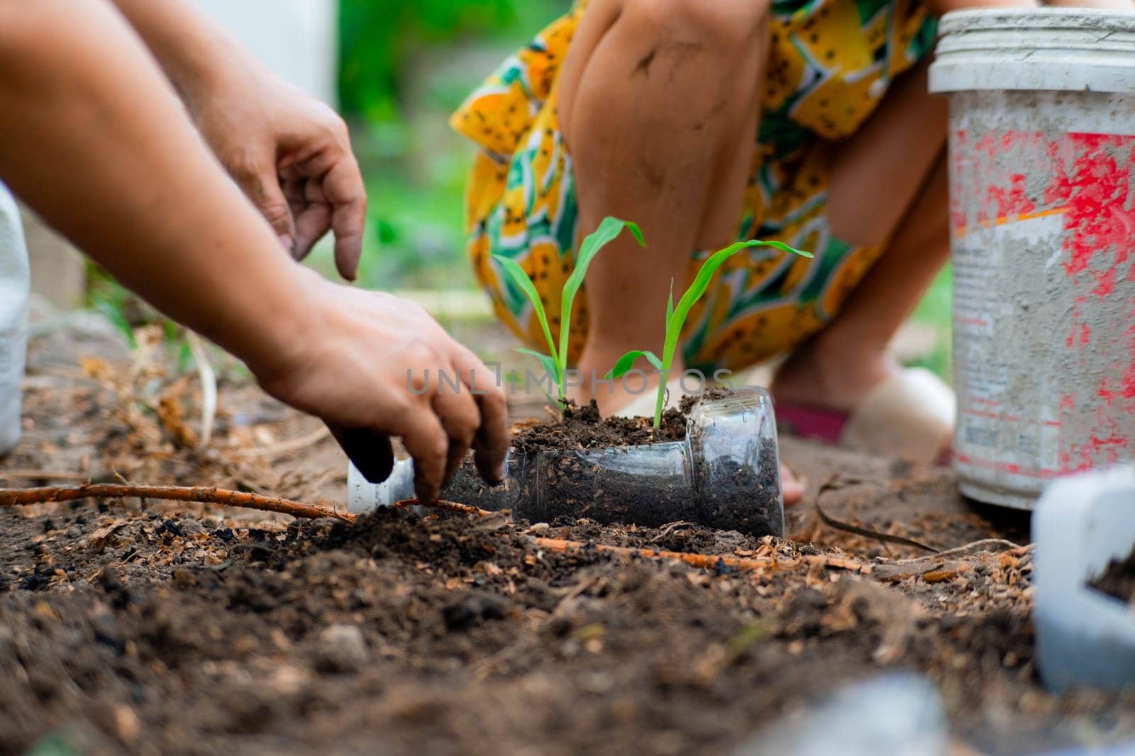 Little girl and mom grow plants in pots from recycled water bottles in the backyard. Recycle water bottle pot, gardening activities for children. Recycling of plastic waste