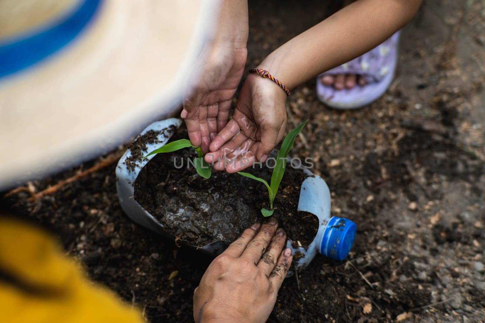 Little girl and mom grow plants in pots from recycled water bottles in the backyard. Recycle water bottle pot, gardening activities for children. Recycling of plastic waste by TEERASAK