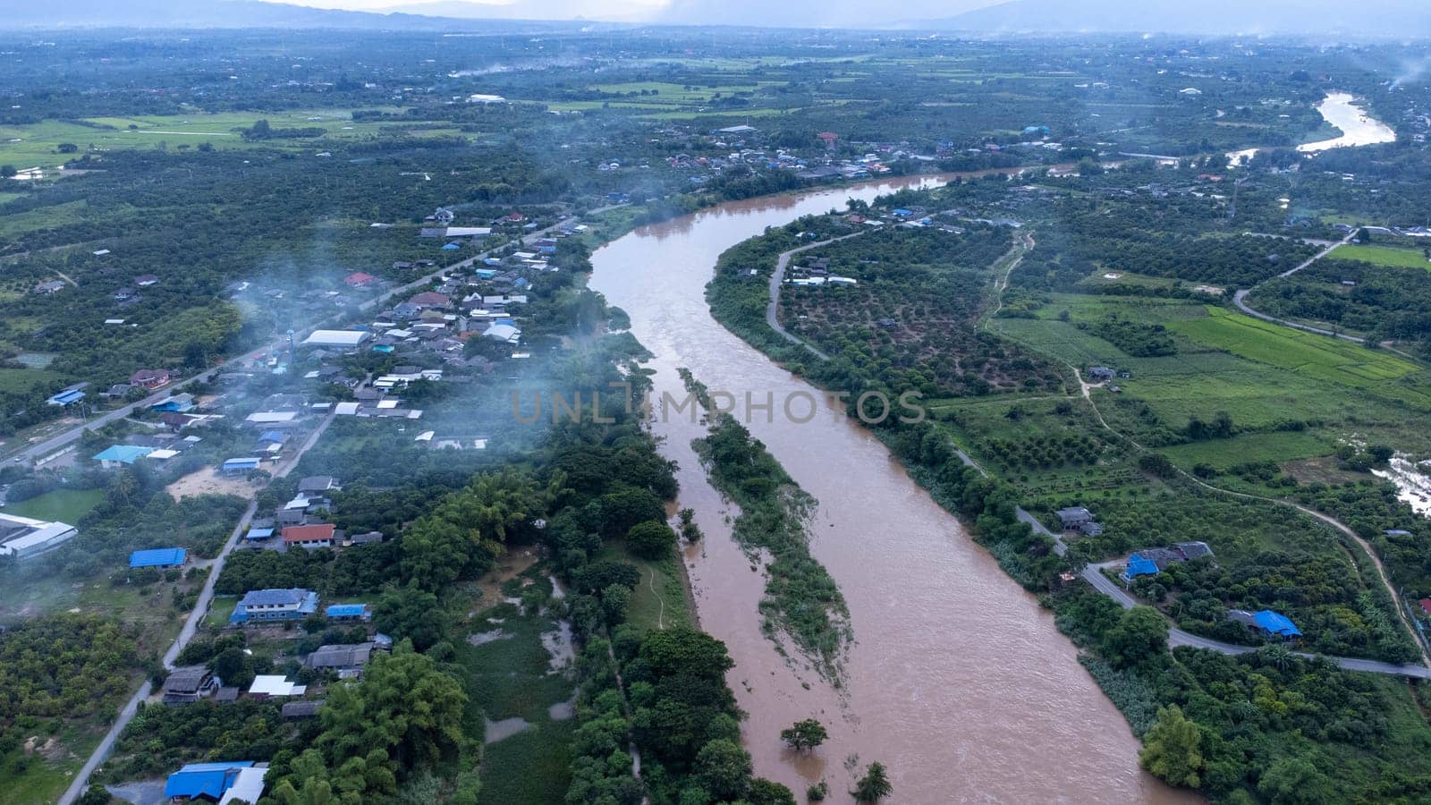 Aerial view of the Ping River across rice fields and rural villages during sunset. Views of Chiang Mai villages and the Ping River from a drone.