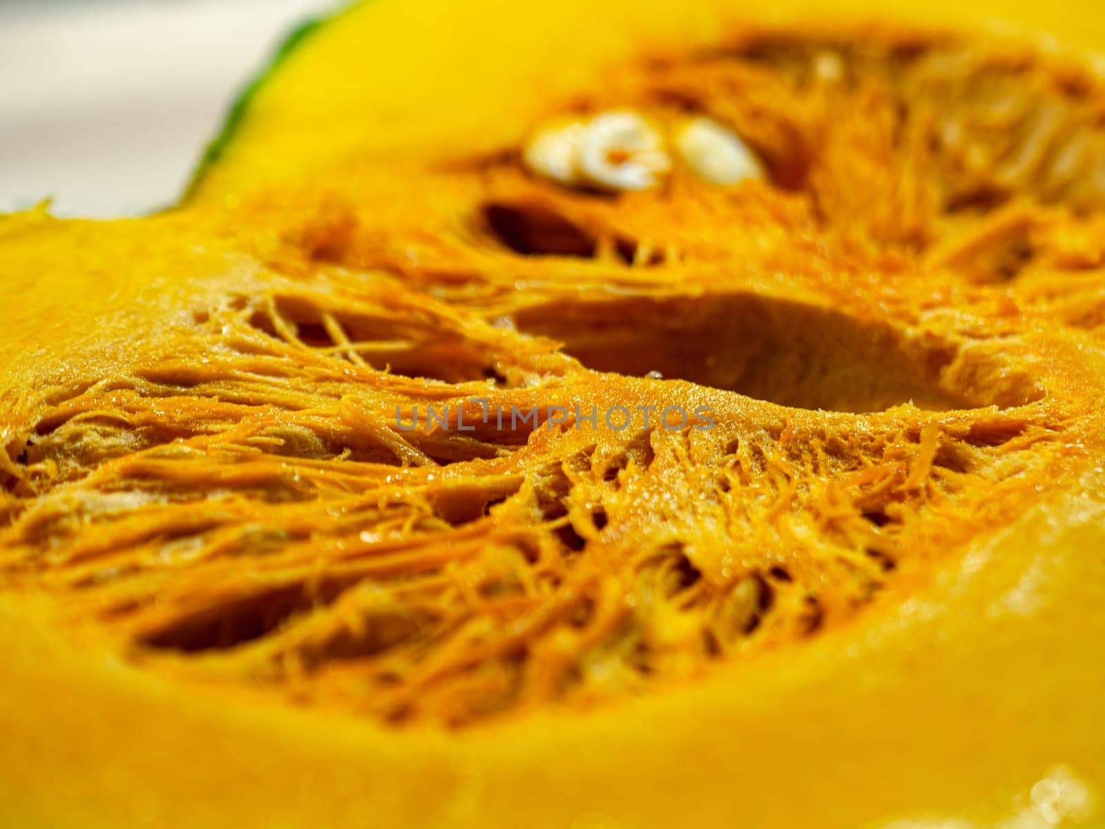Vivid close-up of thick fresh pumpkin slice on wood table. Smooth orange skin with drops of water glistening on surface. Soft natural light illuminates texture and color of ripe flesh in great detail. Shallow depth of field keeps ridges, seeds, and skin in sharp focus.