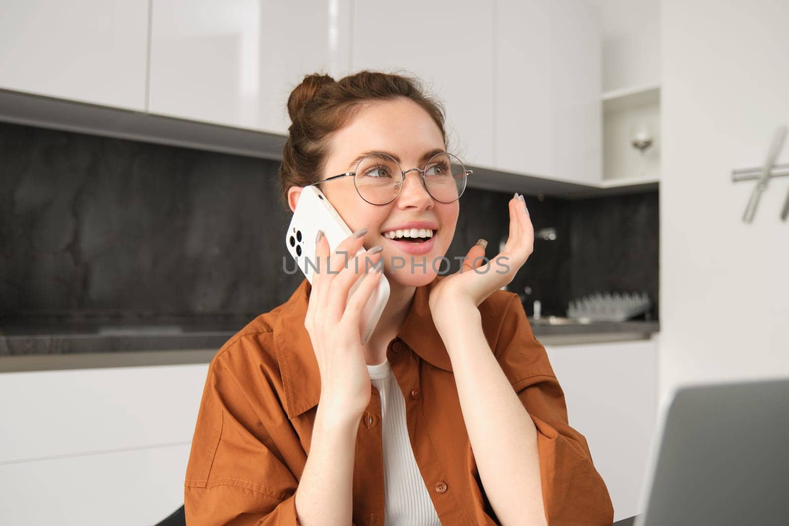 Portrait of young businesswoman, self-employed lady working from home, making phone calls to clients and smiling, using laptop in kitchen by Benzoix