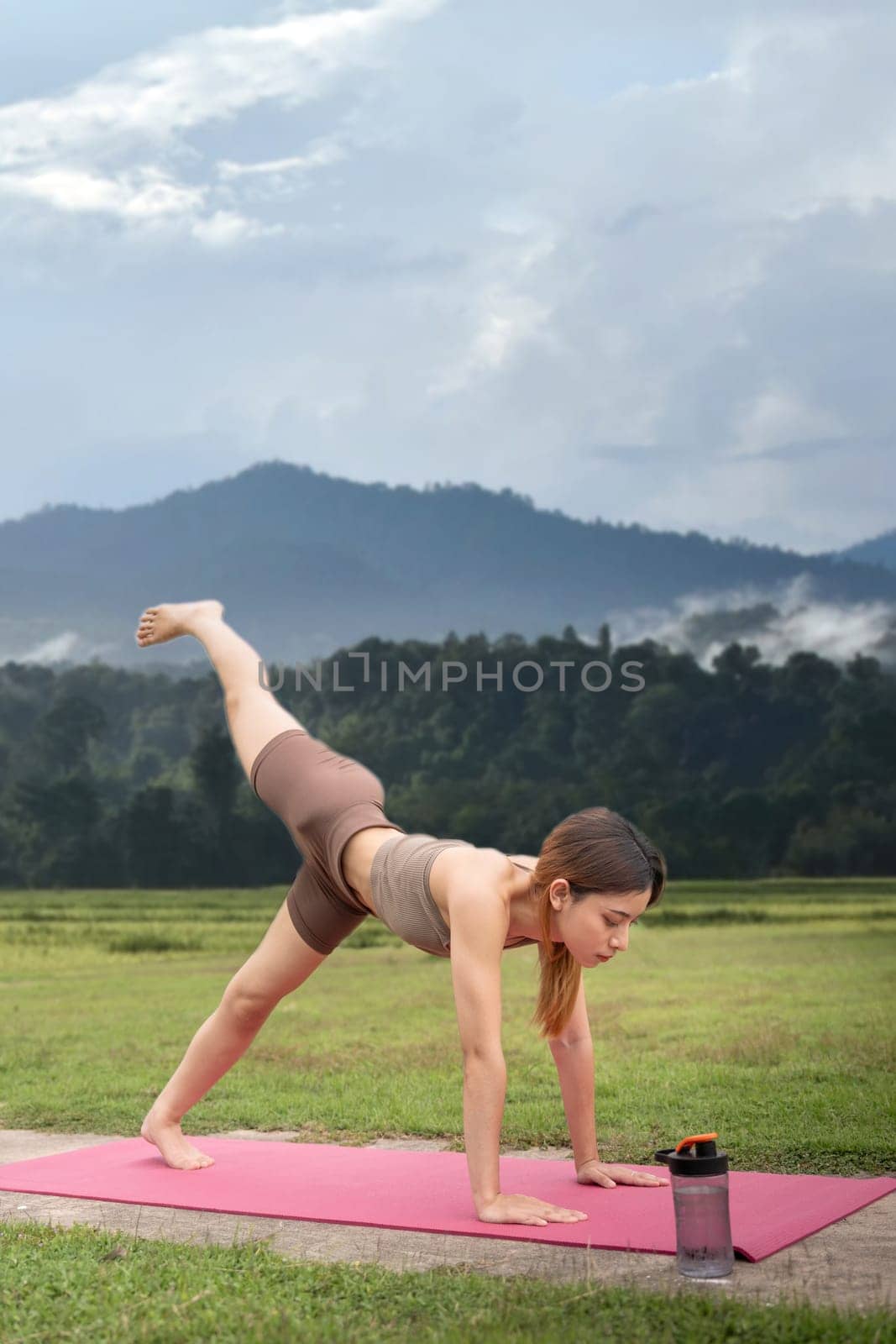 Asian woman sporty practicing yoga at public park outdoor, stretching her body. Healthy active lifestyle.
