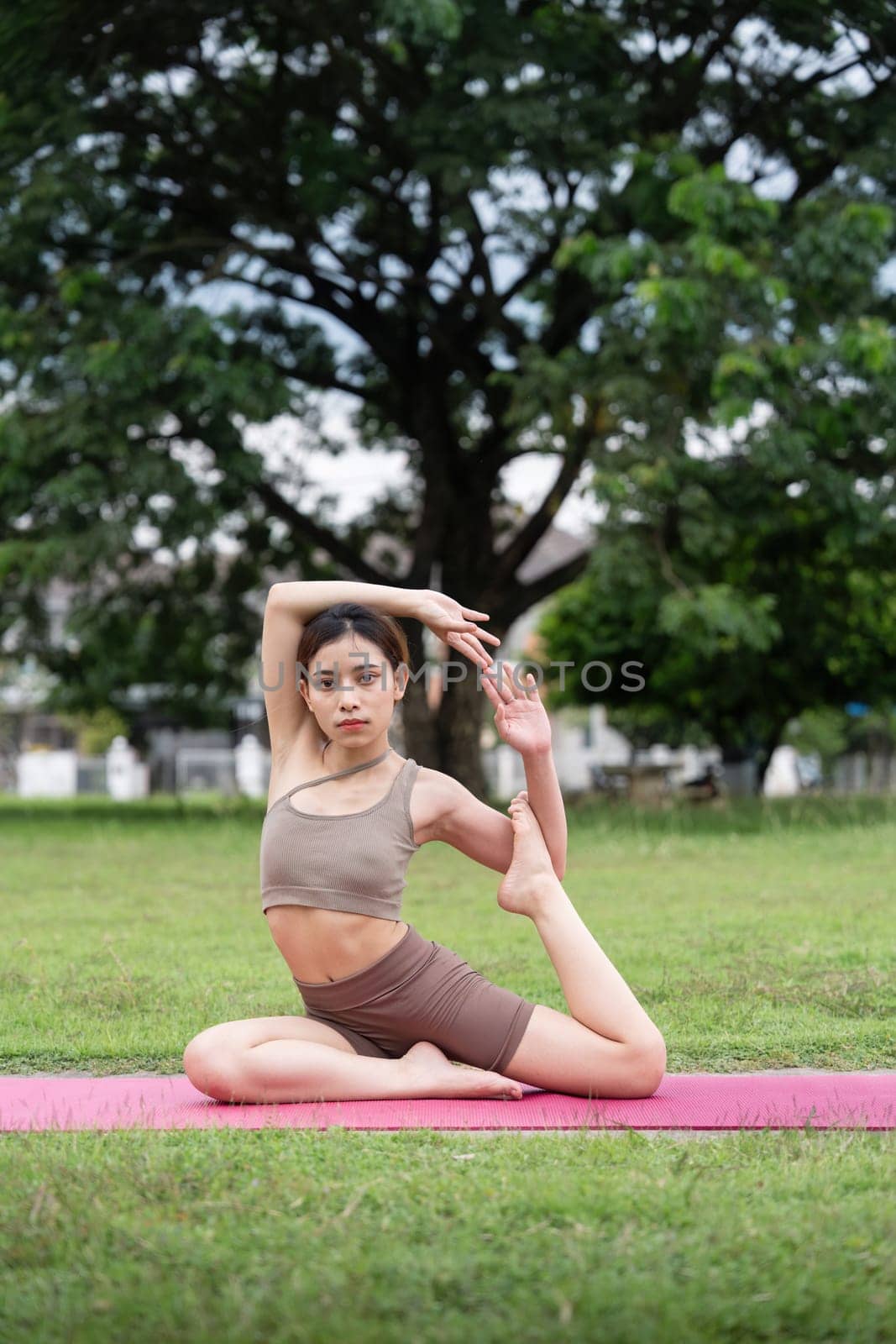 Asian woman sporty practicing yoga at public park outdoor, stretching her body. Healthy active lifestyle by nateemee
