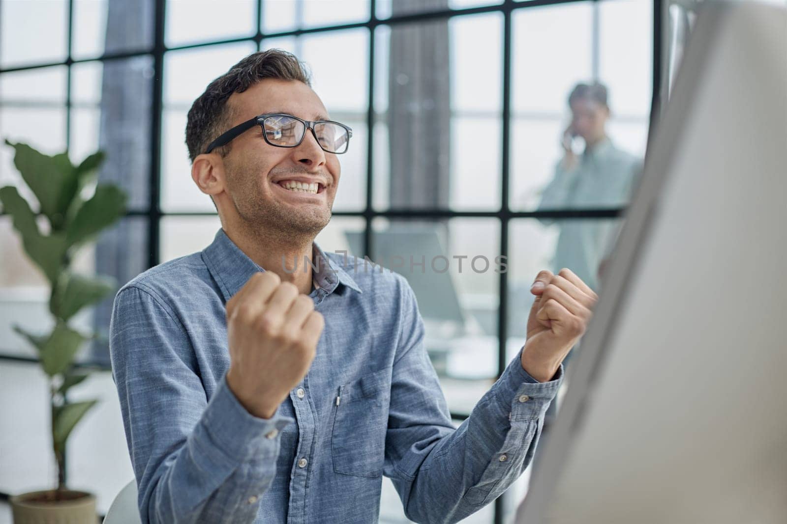 Happy businessman rejoicing success at workplace in office, looking at laptop screen with euphoric expression.