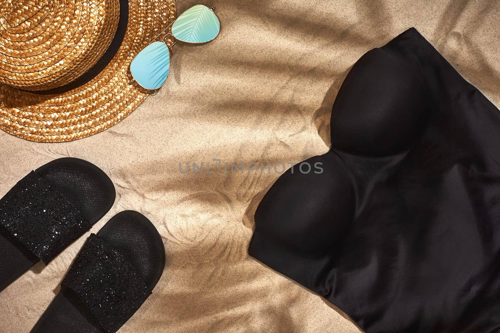 Women's beach accessories or summer outfit on sand background. Shadow from a palm leaf. Top view. Still life. Copy space. Flat lay