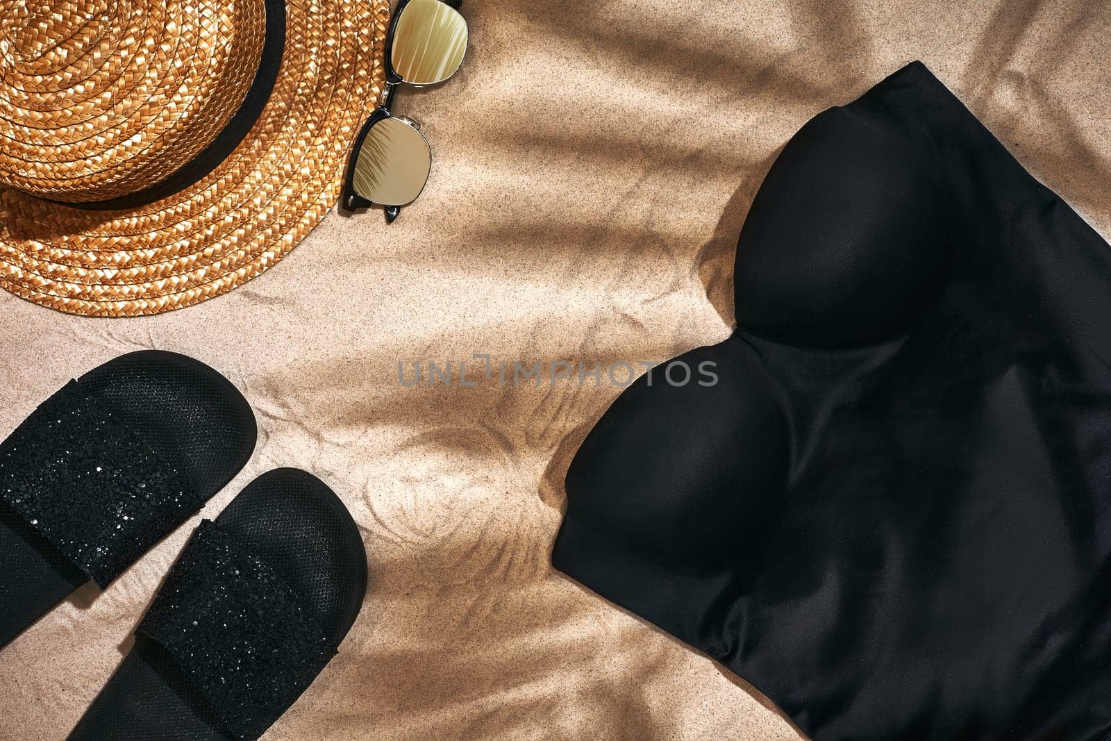 Sandal, straw hat and sunglasses on a sandy background with a shadow from a palm leaf, top view. Still life. Copy space. Flat lay.
