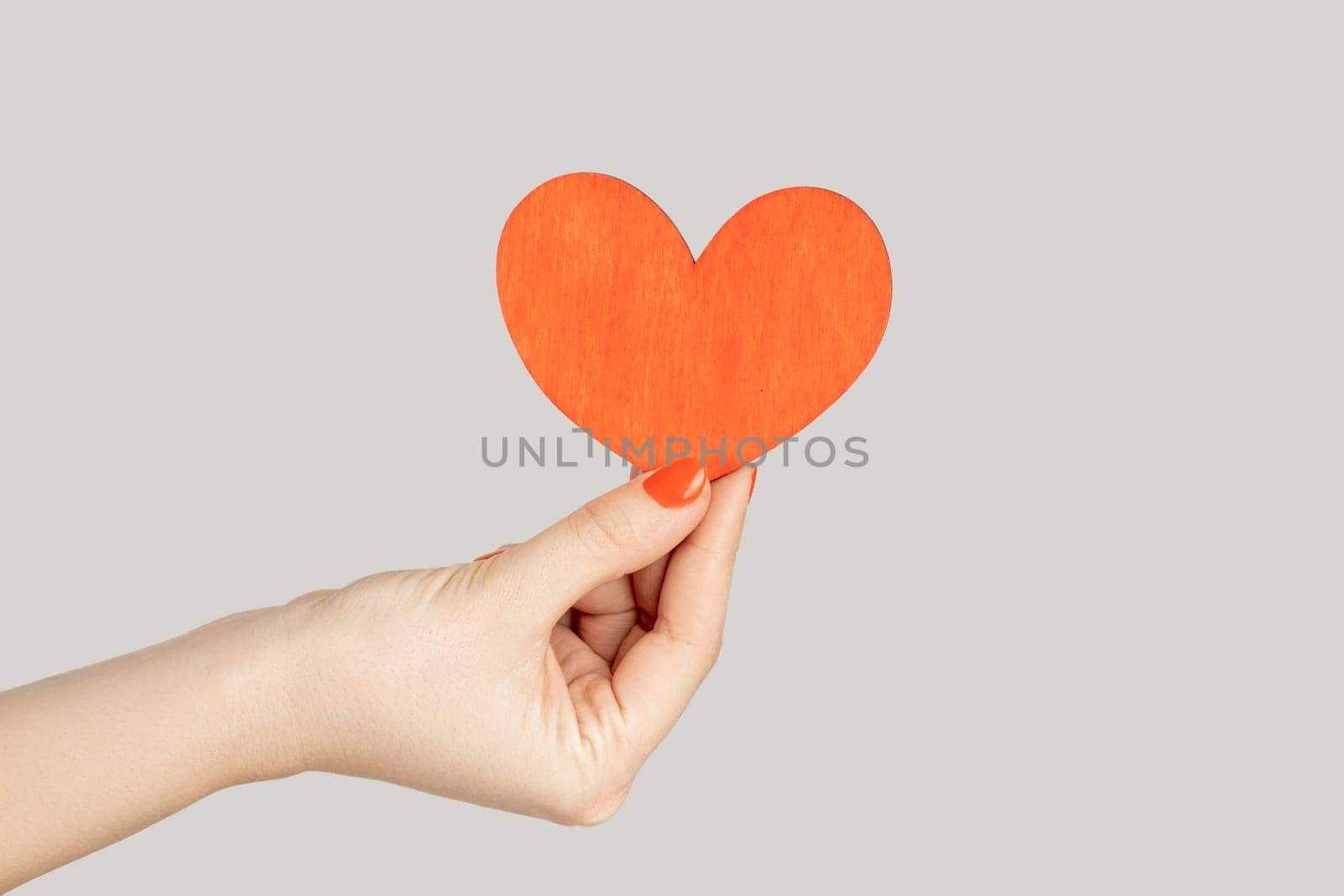 I love you. Closeup of woman hand showing little red paper heart symbol of love and devotion. Indoor studio shot isolated on gray background.