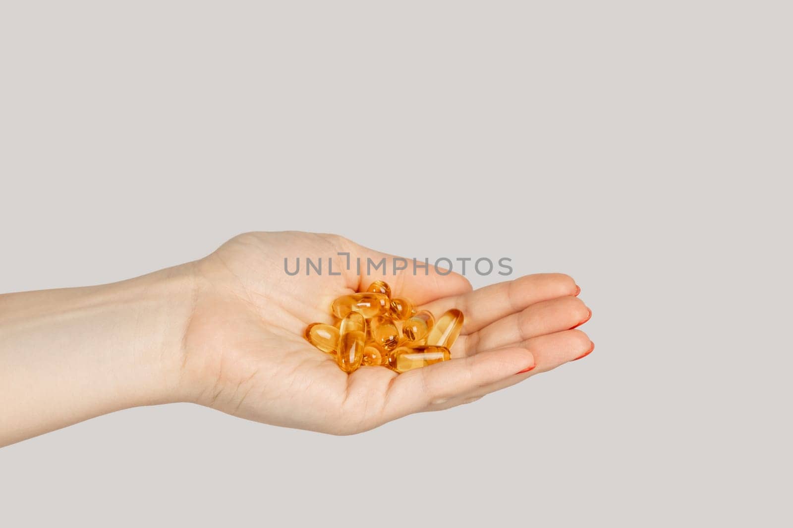 Closeup of woman hand handful of pills capsules, nutritional supplement, vitamins, medicine. Indoor studio shot isolated on gray background.