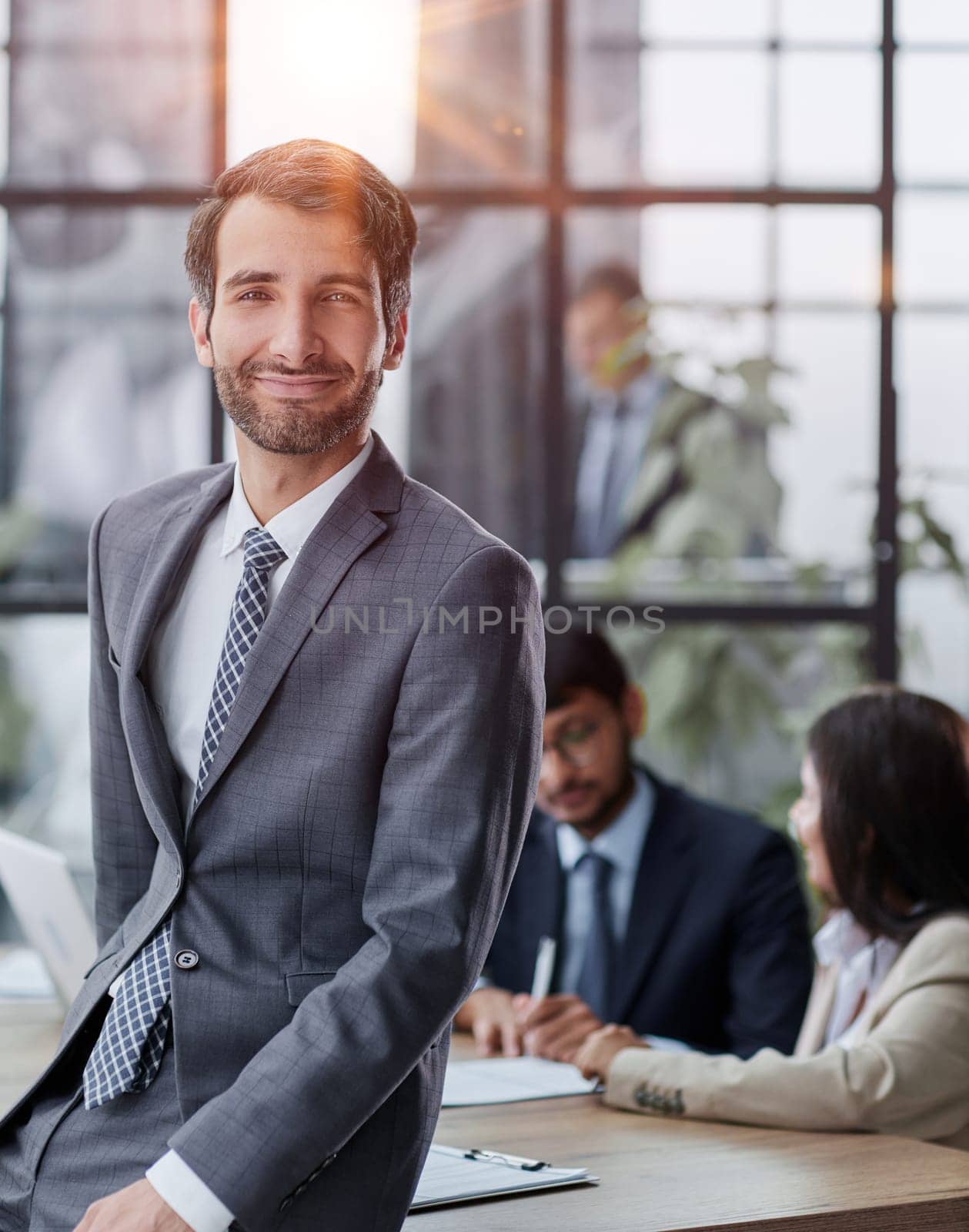 professional businessman, executive director of the company, sitting at the table in the office, with colleagues in the background