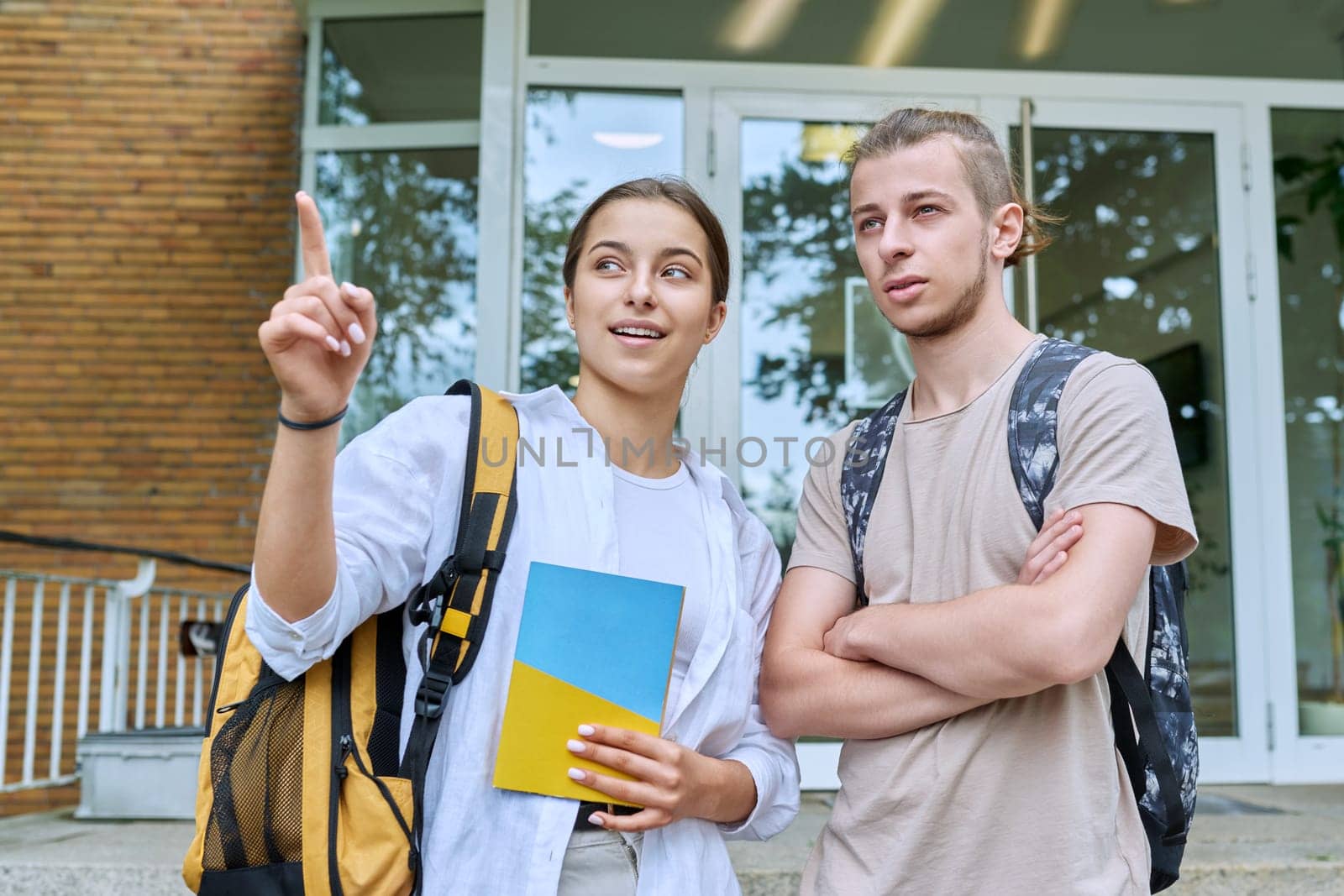 Meeting of two teenage students, guy and girl, outdoors near educational building. Friendship, communication, education, high school college concept