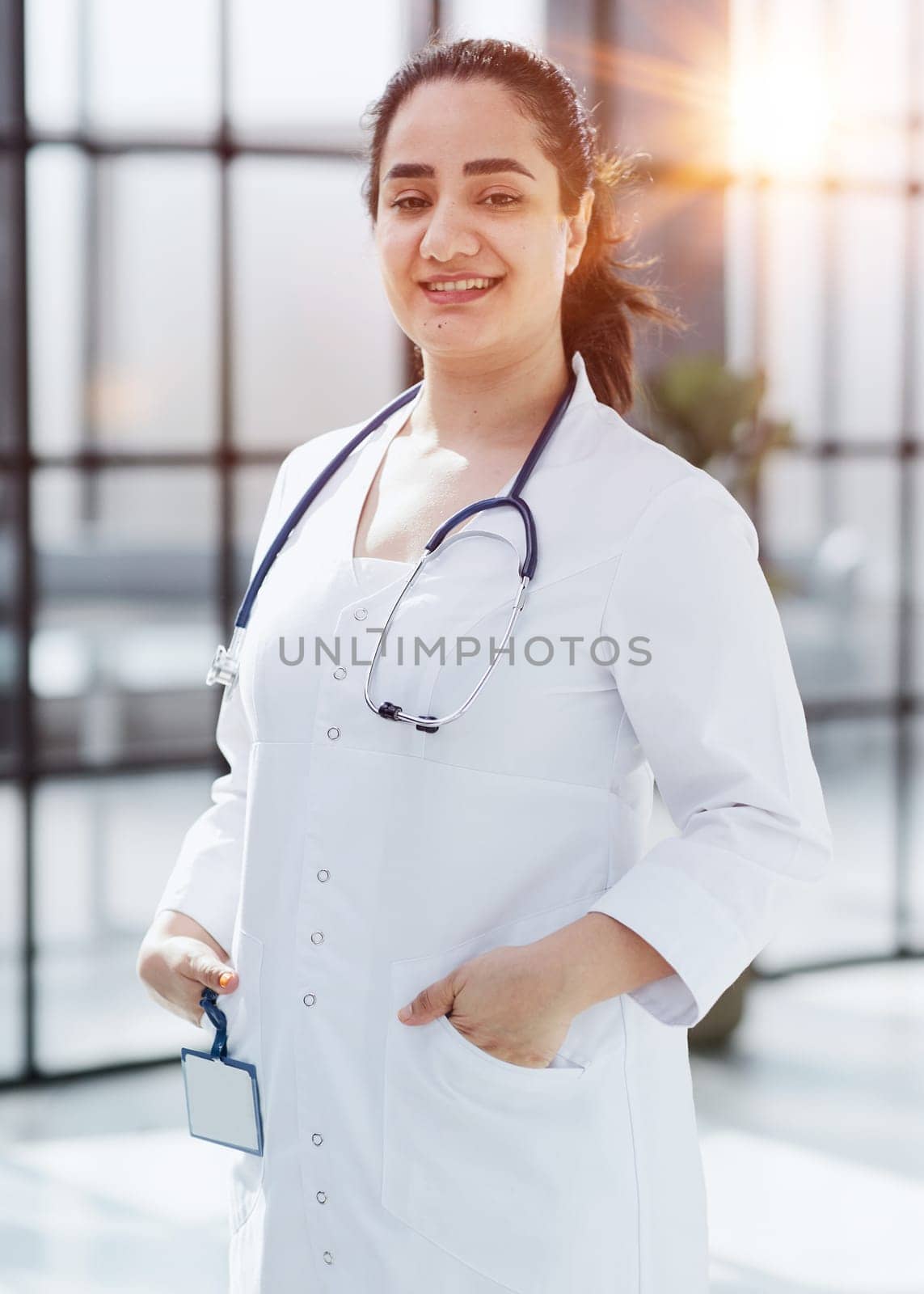 Dentist woman standing with crossed arms. Confident dentist standing in a hospital corridor in a white coat. by Prosto