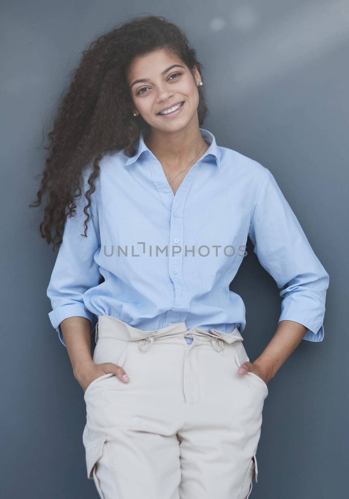 Smiling attractive young business woman in blue shirt posing on gray background by Prosto