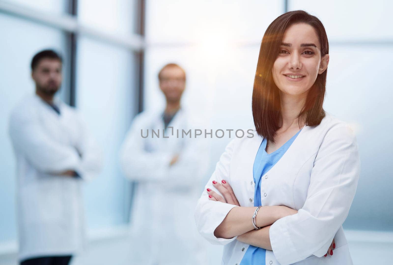 Smiling female doctor in lab coat with arms crossed against by Prosto