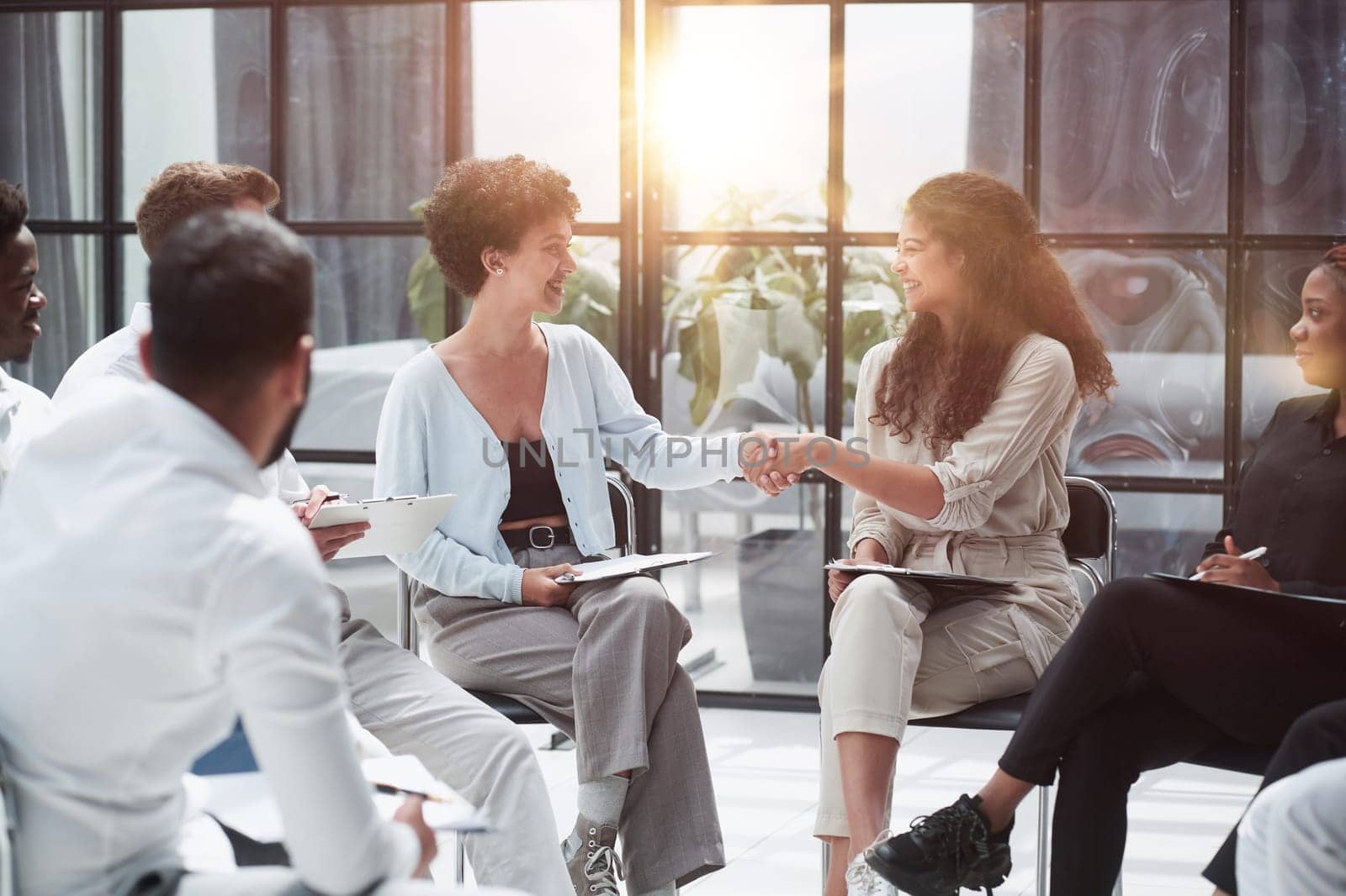 Welcome aboard. Group of business people sitting on a chair while two people shake hands by Prosto