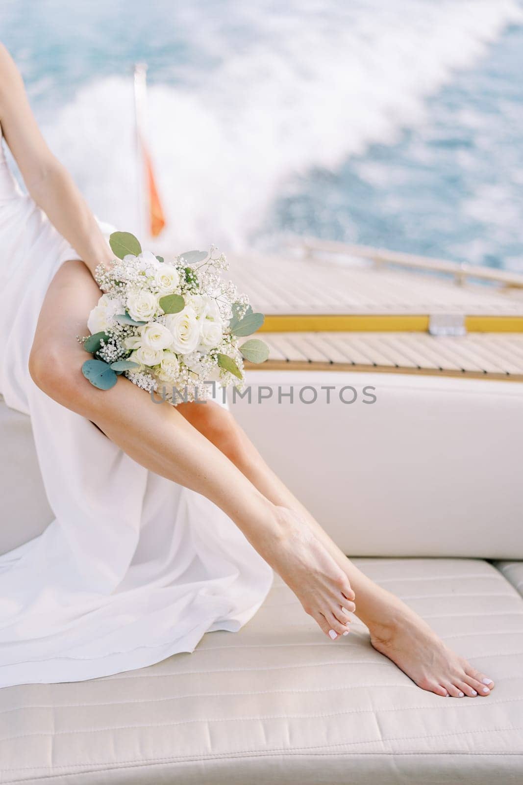 Bride with a bouquet sits on board a yacht sailing on the sea. Cropped. Faceless. High quality photo