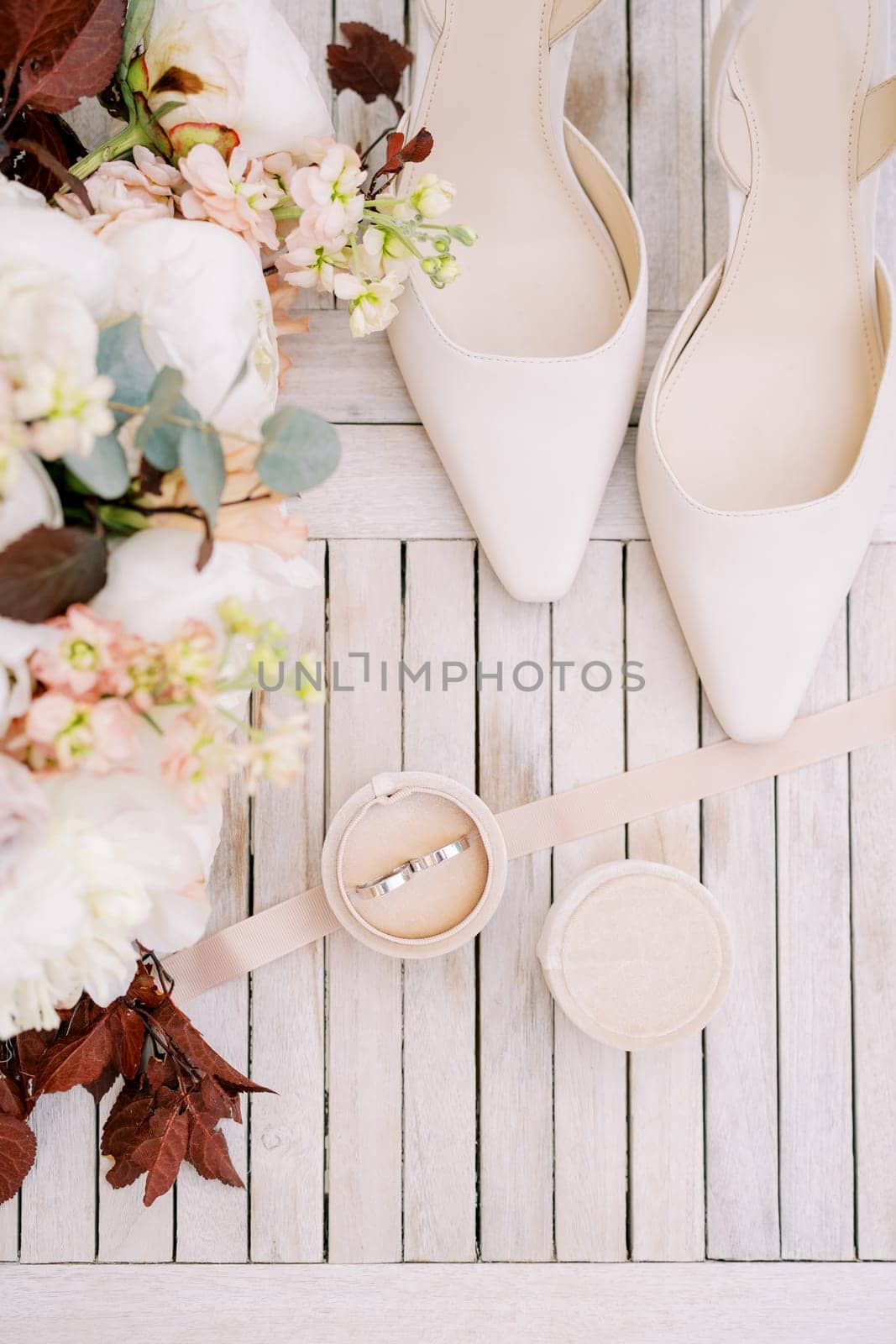 Wedding rings in a box stand on the table near the bride shoes and a bouquet of flowers. Top view. High quality photo
