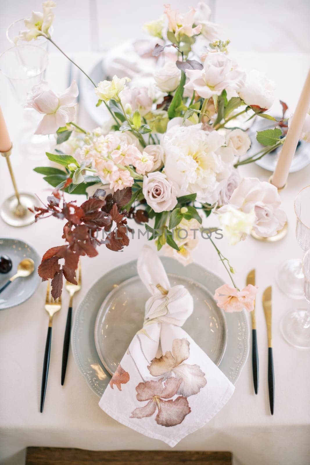 Knotted napkin lies on a plate near a bouquet on a festive table by Nadtochiy