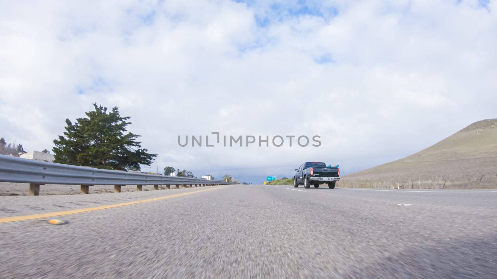Santa Maria, California, USA-December 6, 2022-On a crisp winter day, a car cruises along the iconic Highway 101 near San Luis Obispo, California. The surrounding landscape is brownish and subdued, with rolling hills and patches of coastal vegetation flanking the winding road.