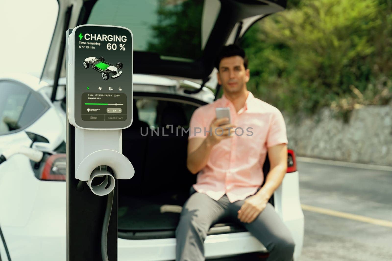 EV car recharging battery from outdoor EV charger display battery status on blur background of man using smartphone with natural scenic as concept of eco-friendly travel with clean energy. Perpetual
