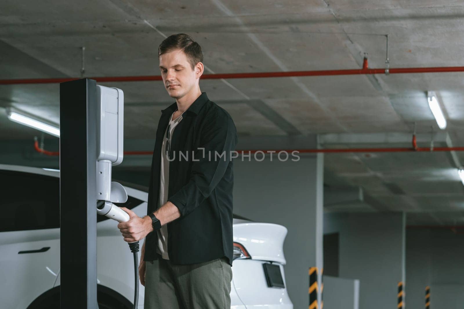 Young man travel with EV electric car to shopping center parking lot charging in downtown city showing urban sustainability lifestyle by green clean rechargeable energy of electric vehicle innards