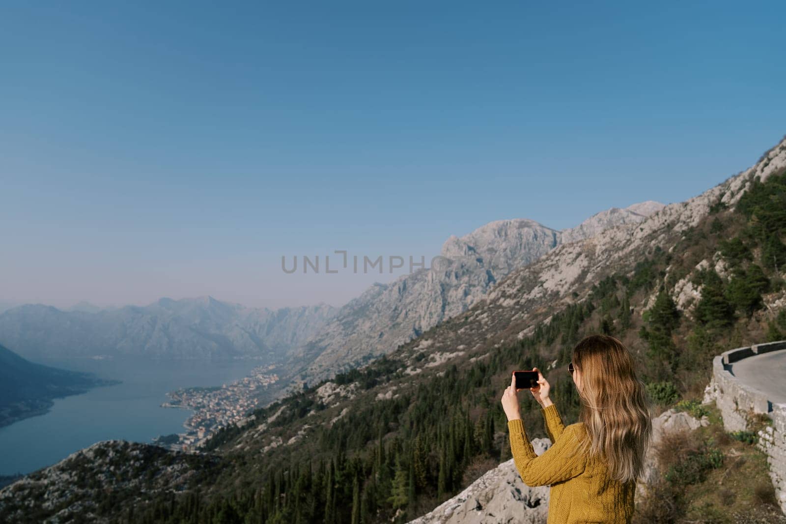 Woman stands on a mountain and shoots a view of the Bay of Kotor with a smartphone. Montenegro. Side view. High quality photo