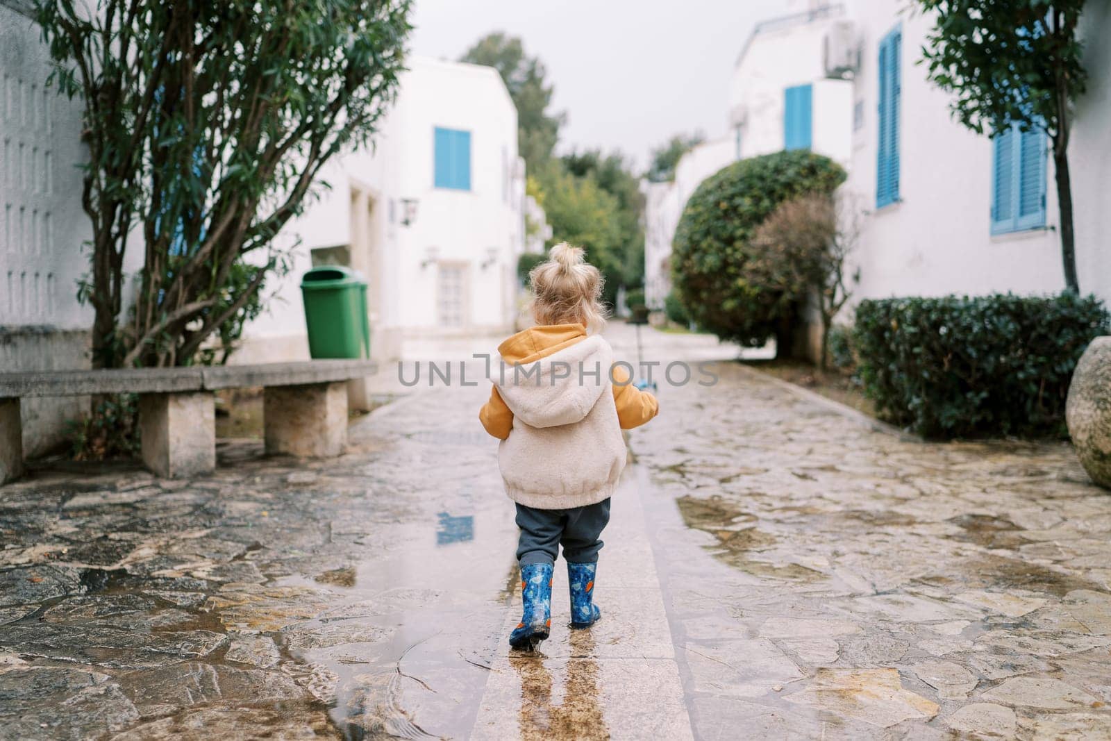Little girl walks through the puddles in the courtyard. Back view. High quality photo