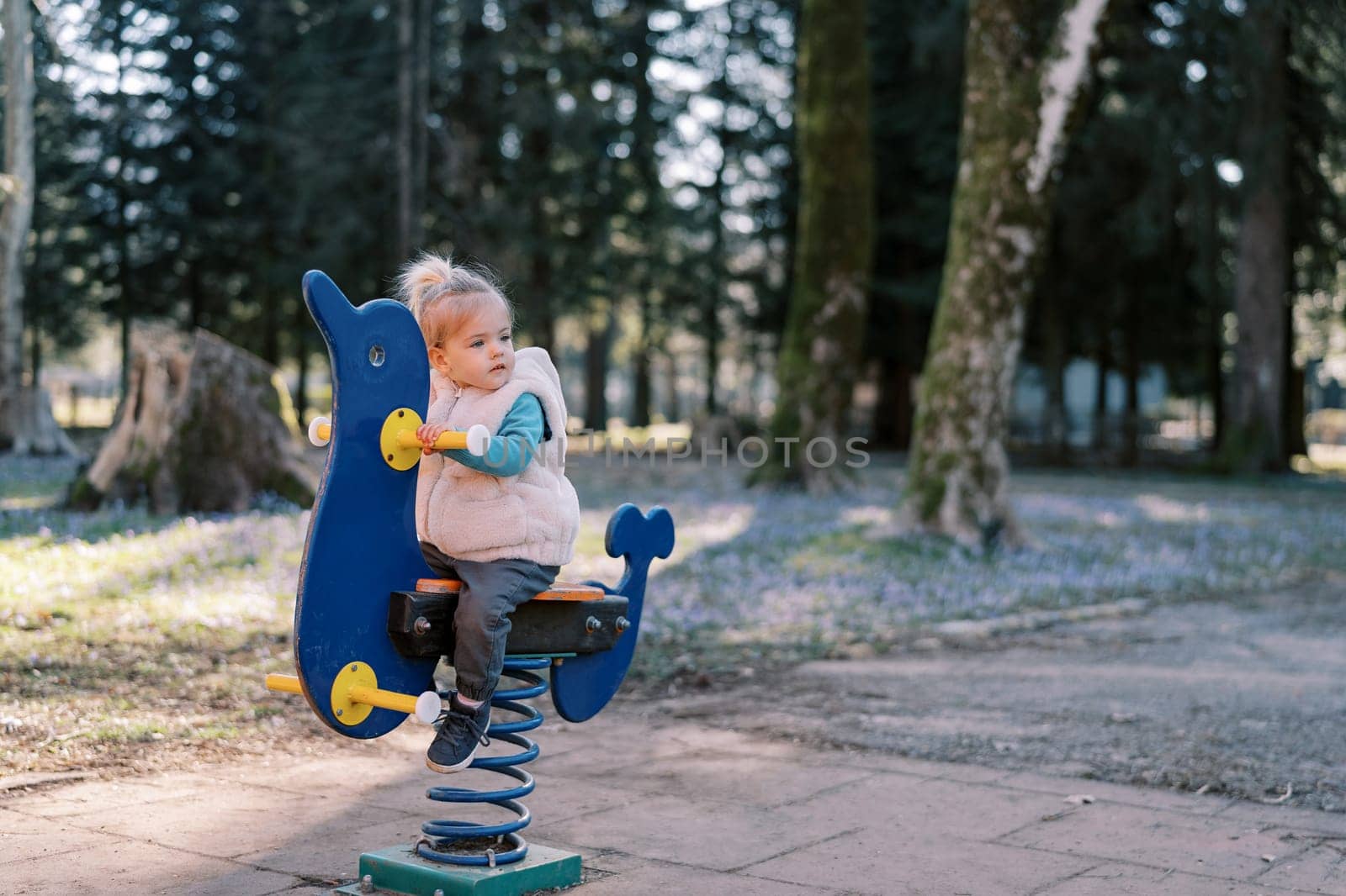 Little girl sits on a spring swing and looks away. High quality photo