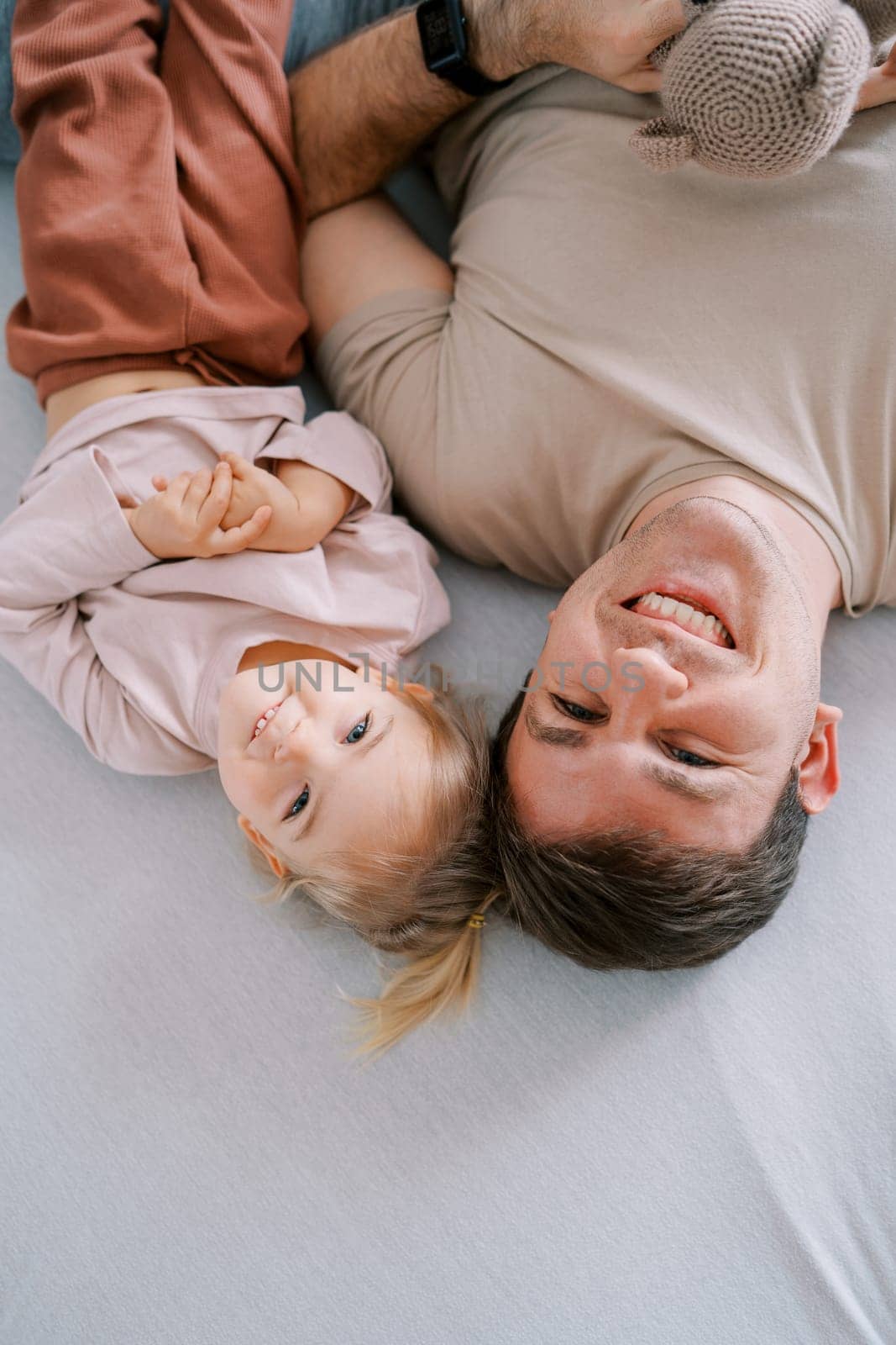 Laughing dad with a little girl lie upside down on the bed. Top view. High quality photo