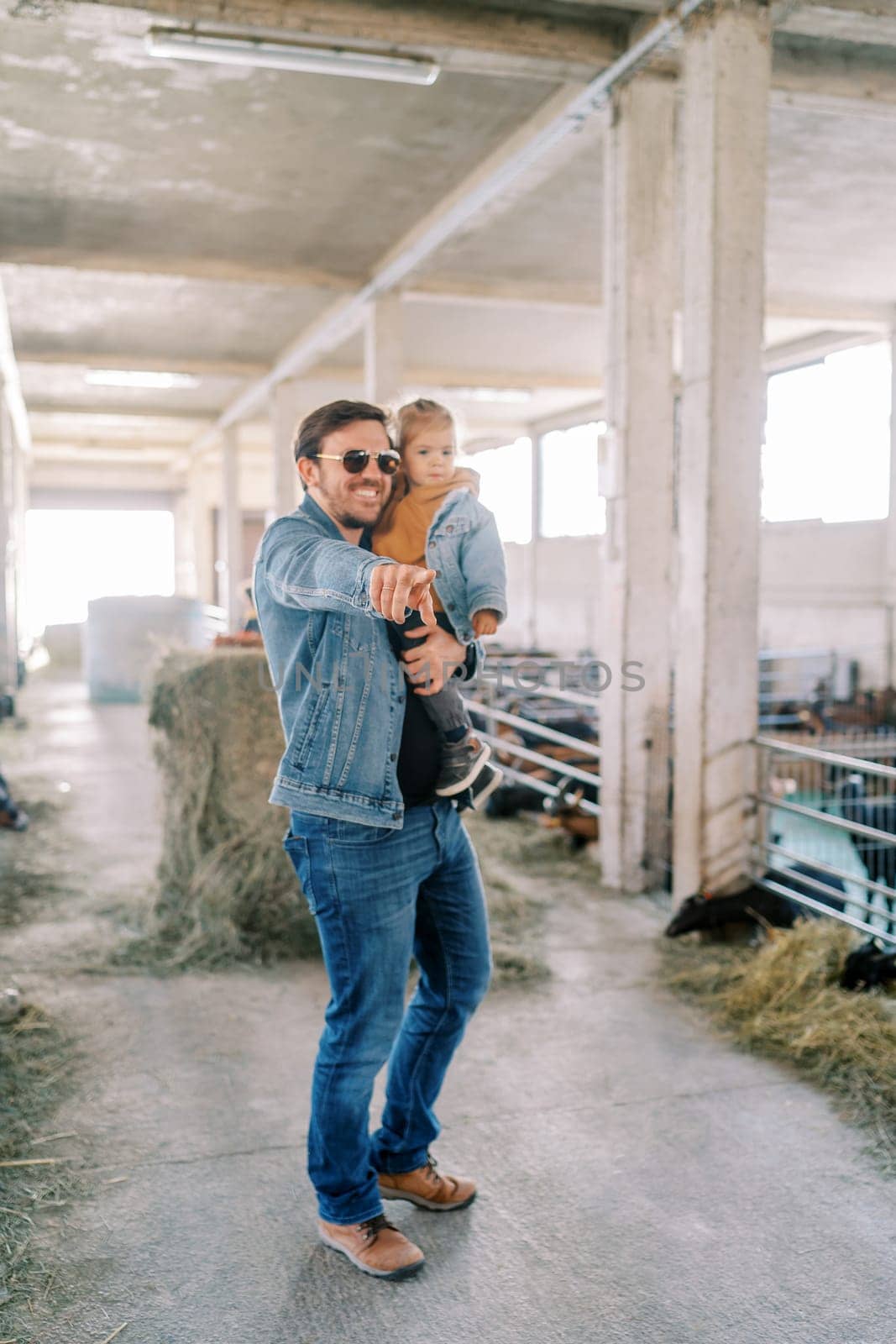 Smiling dad pointing into the distance to a little girl in his arms while standing on a farm. High quality photo