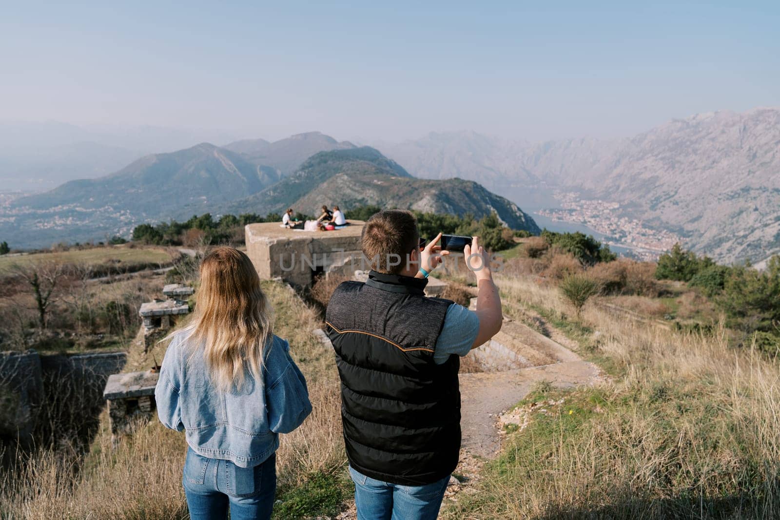 Woman stands next to a man filming the ruins of a fort in the mountains on a mobile phone. Back view. High quality photo