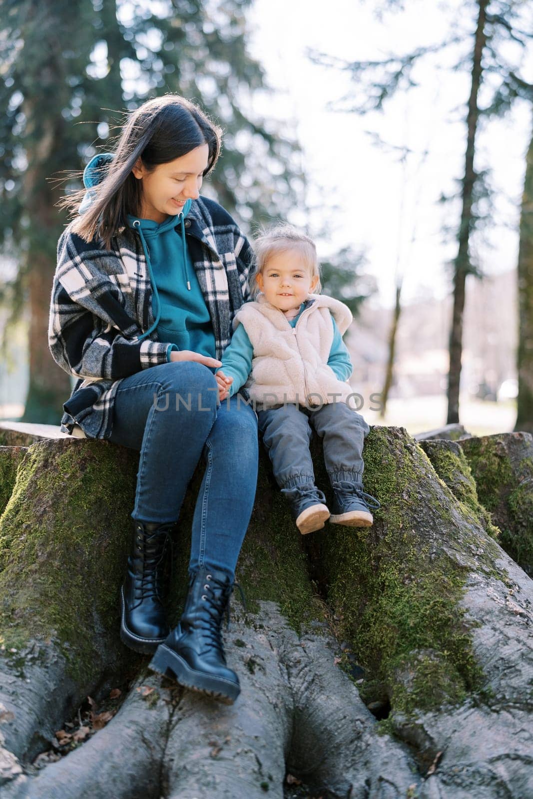 Smiling mother with a little girl are sitting on a stump covered with green moss in the forest. High quality photo