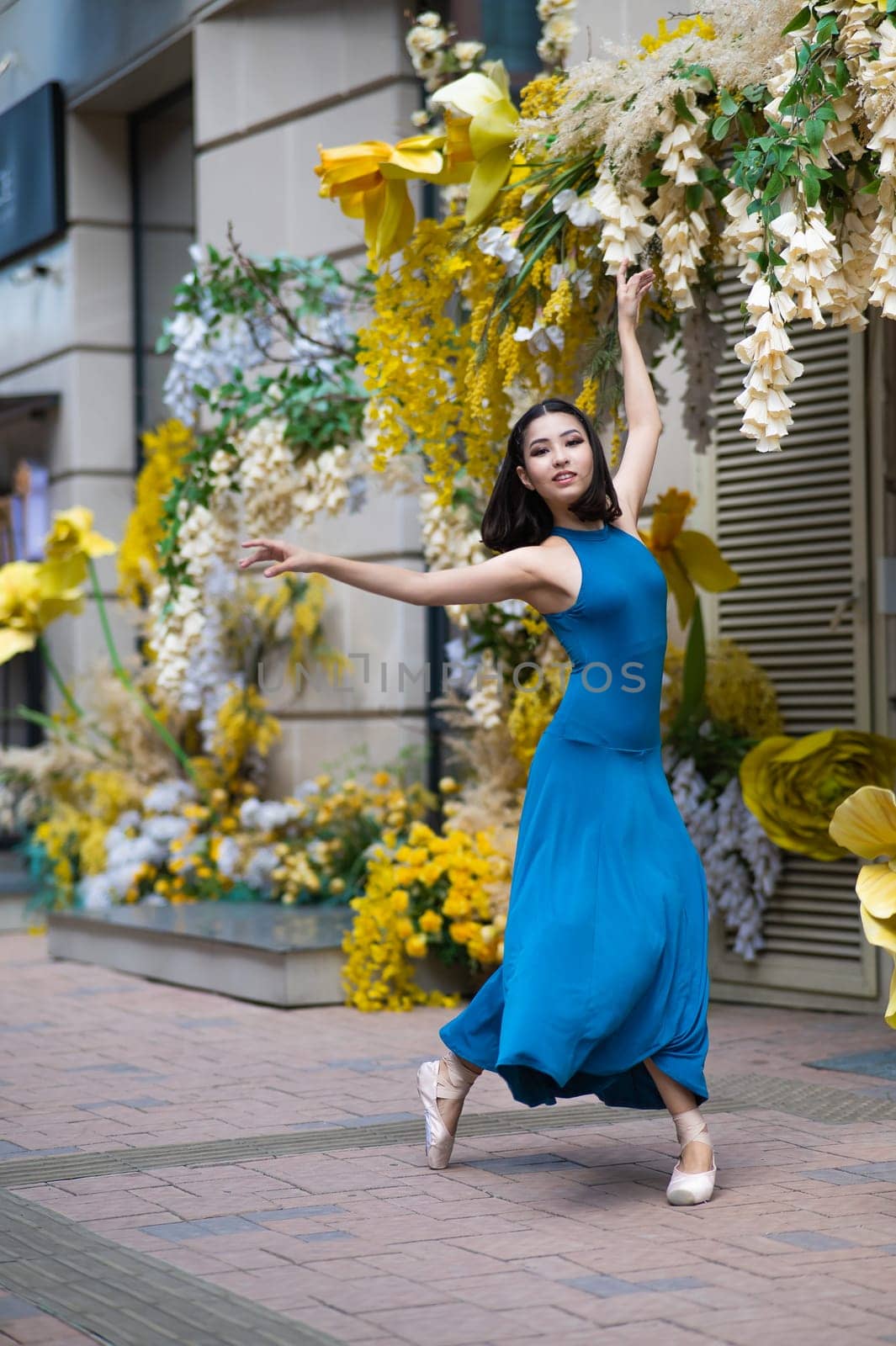 Beautiful Asian ballerina dances against the background of a building decorated with flowers. Vertical photo. by mrwed54