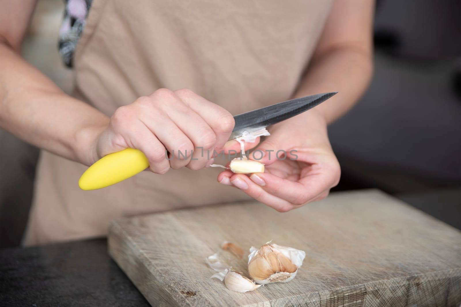 A woman cuts garlic with a knife close-up. Cutting garlic for salad or as an aromatic spice for meat. by SERSOL