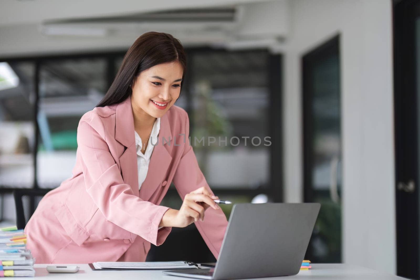 businesswomen looking at a laptop screen while standing up near her work desk. by wichayada