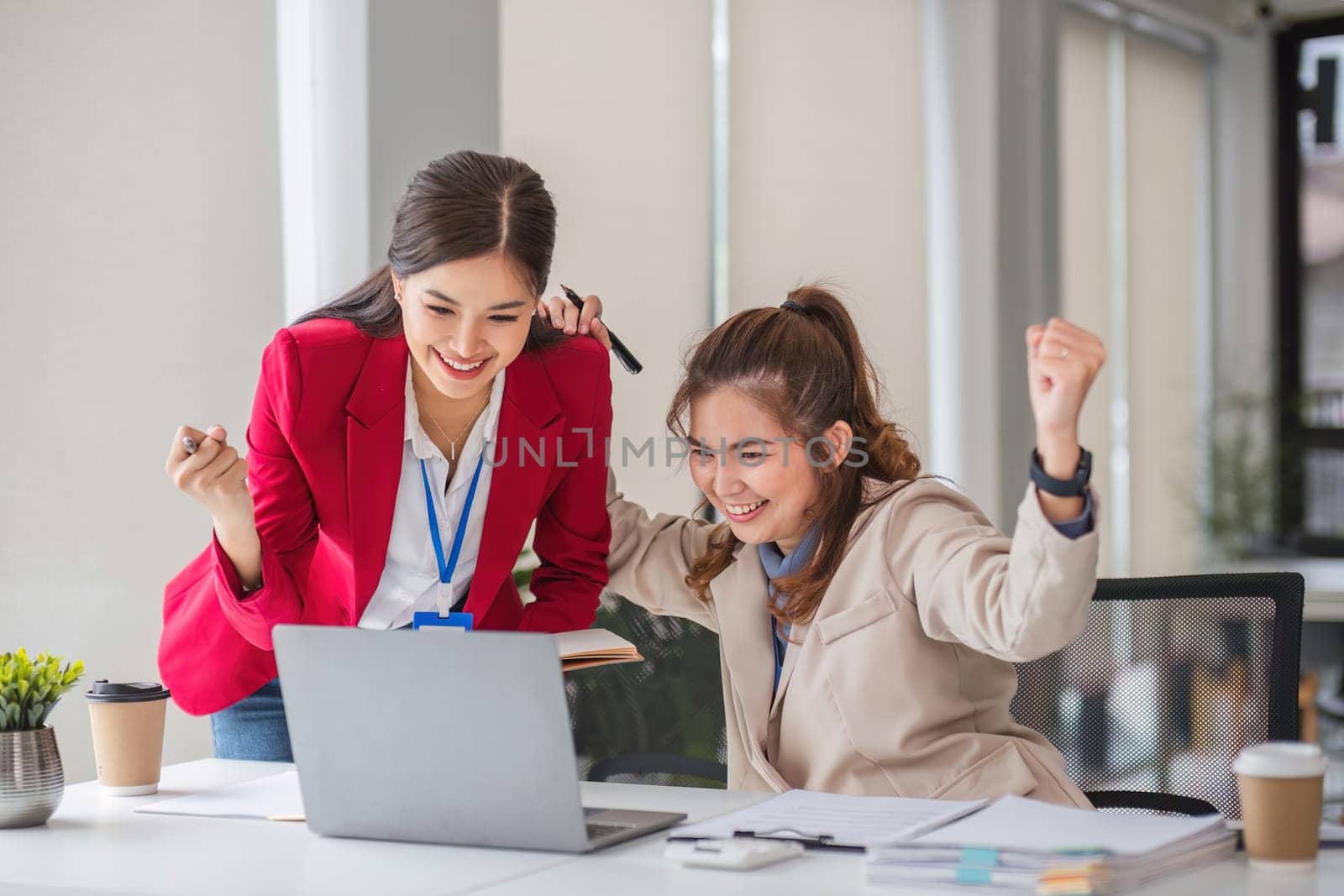 Two Asian businesswoman showing excited expression in front of laptop due to successful results. by wichayada