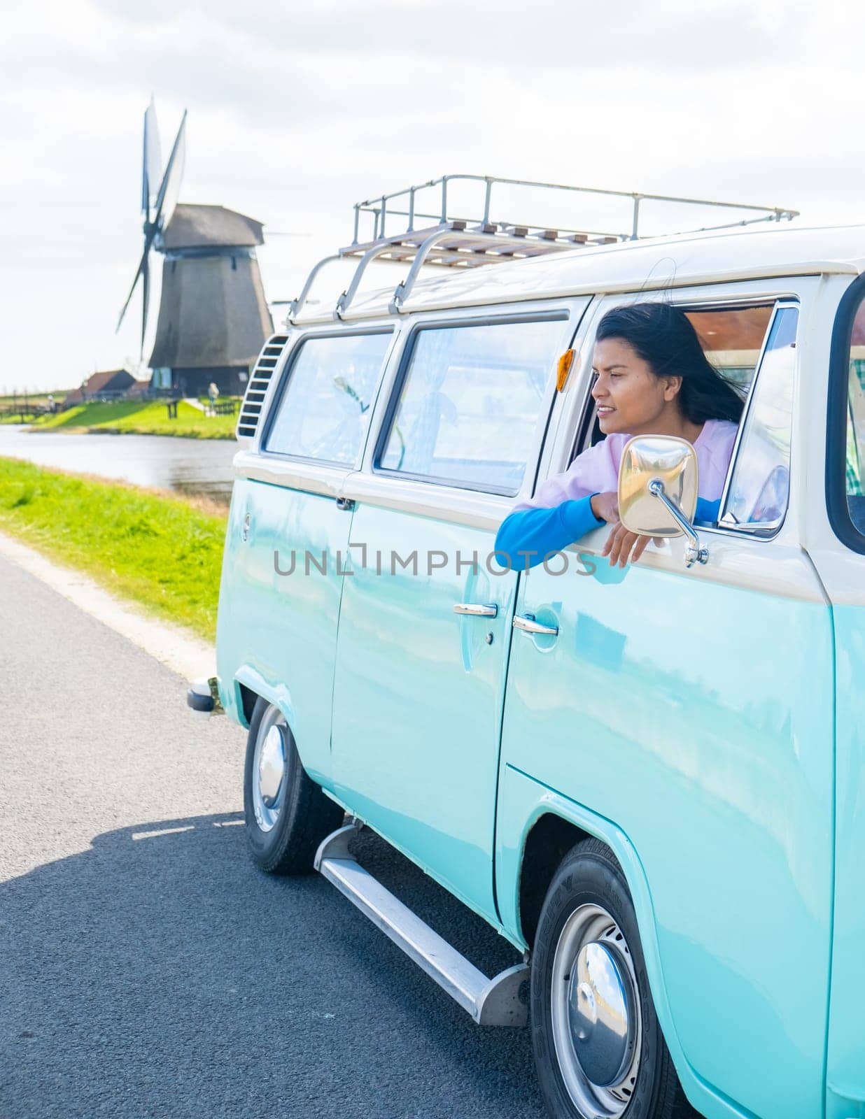 woman doing a road trip with an old vintage car in the Dutch flower bulb region with tulip fields during Spring in the Netherlands, women with a old camper van