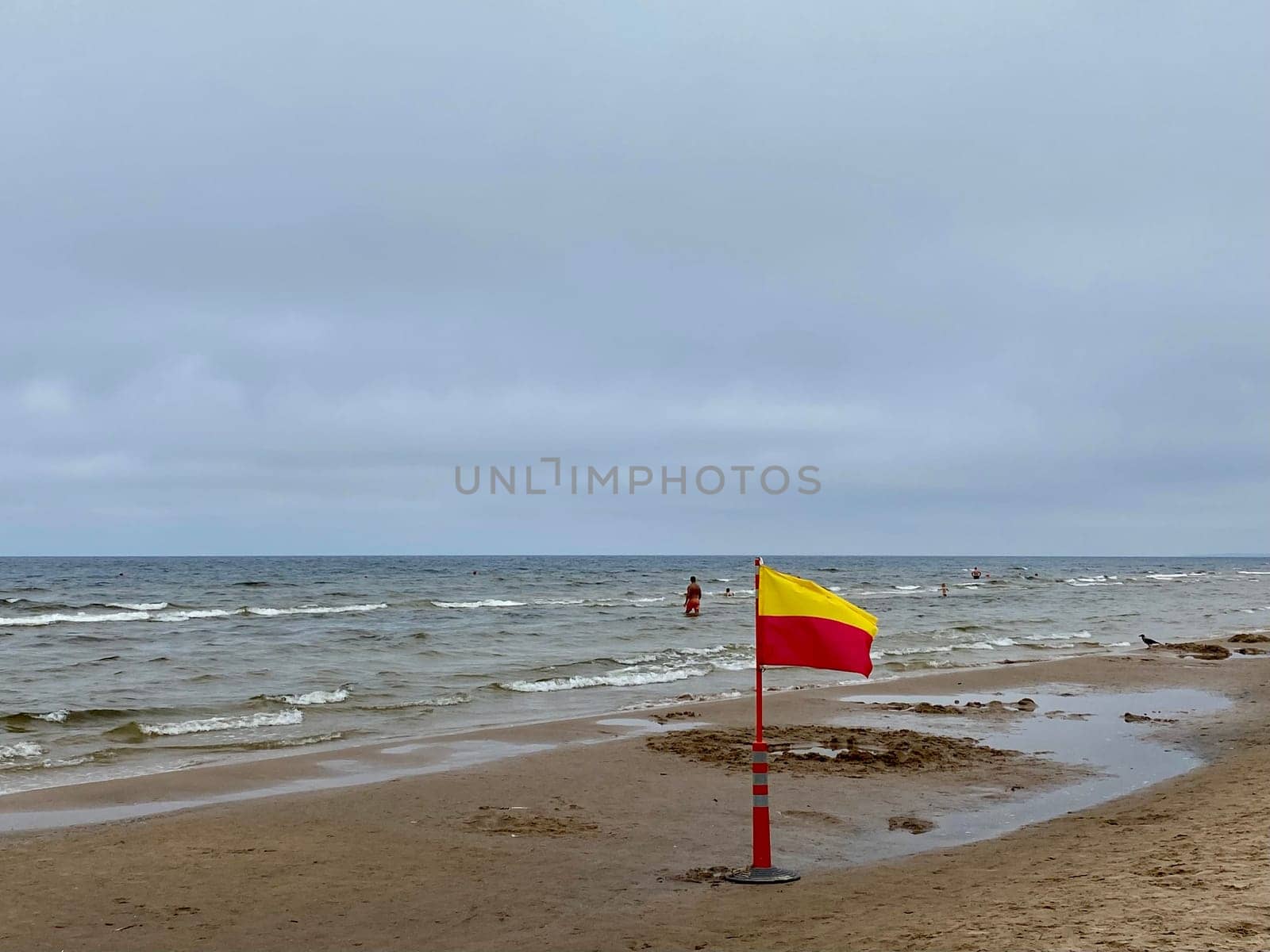 A Yellow and red beach flag, warning flag, lifesaving surf flag, rainy day in the beach, beach storm attention by DailySF