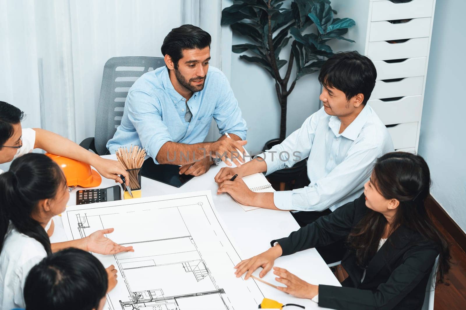 Diverse group of civil engineer and client working together on architectural project, reviewing construction plan and building blueprint at meeting table. Prudent