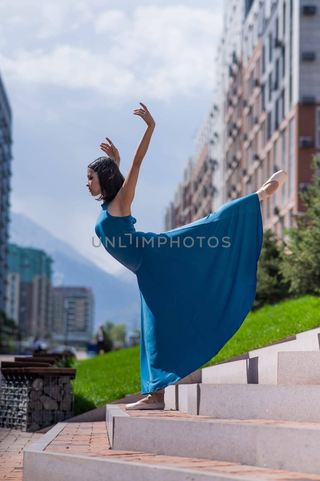 Beautiful Asian ballerina in blue dress posing on stairs outdoors. Urban landscape