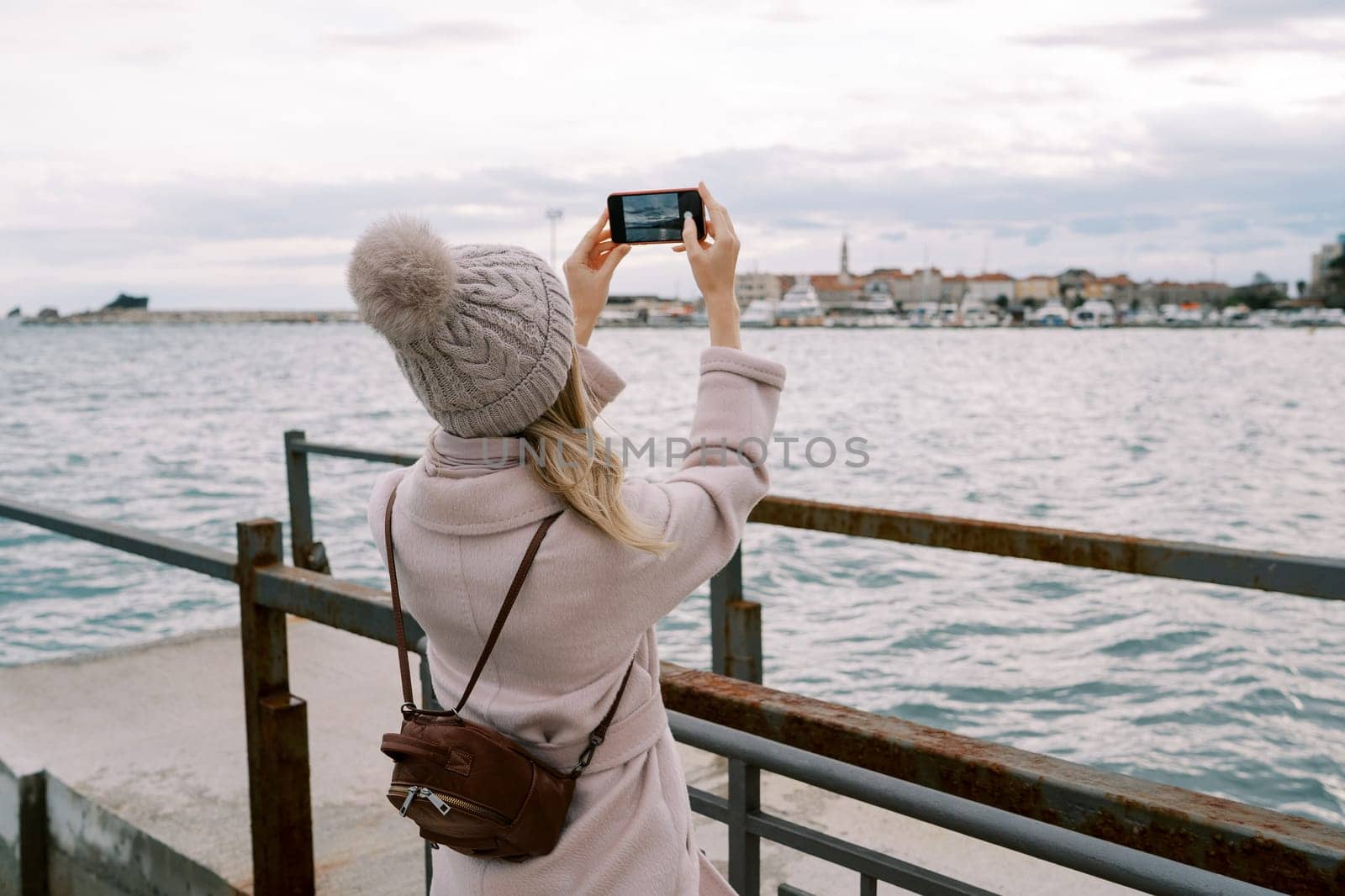 Traveler takes pictures of the coast of a resort town with moored yachts with a smartphone. Back view. High quality photo