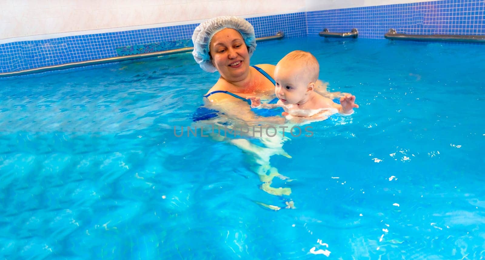 Adorable baby girl enjoying swimming in a pool with her mother early development class for infants teaching children to swim and dive. by kajasja