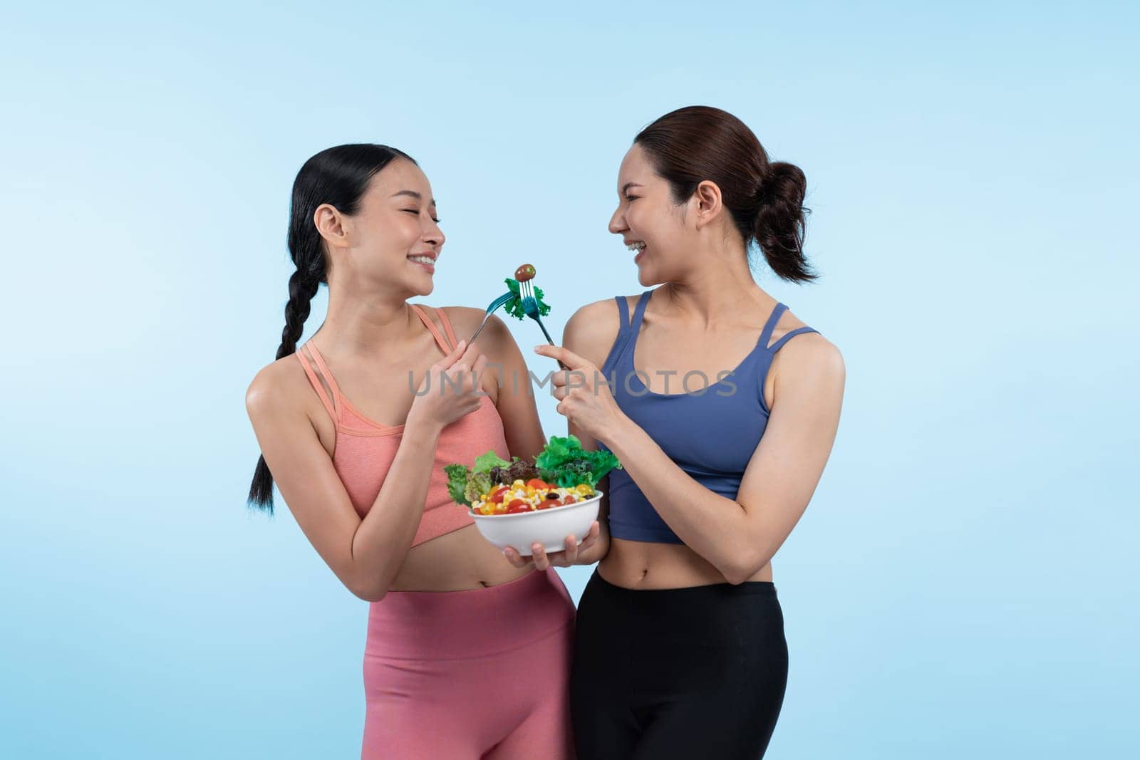 Two young sporty Asian women in sportswear holding salad bowl fill with fruit and vegetable. Natural youthful and fit body lifestyle people with balance nutrition on isolated background. Vigorous