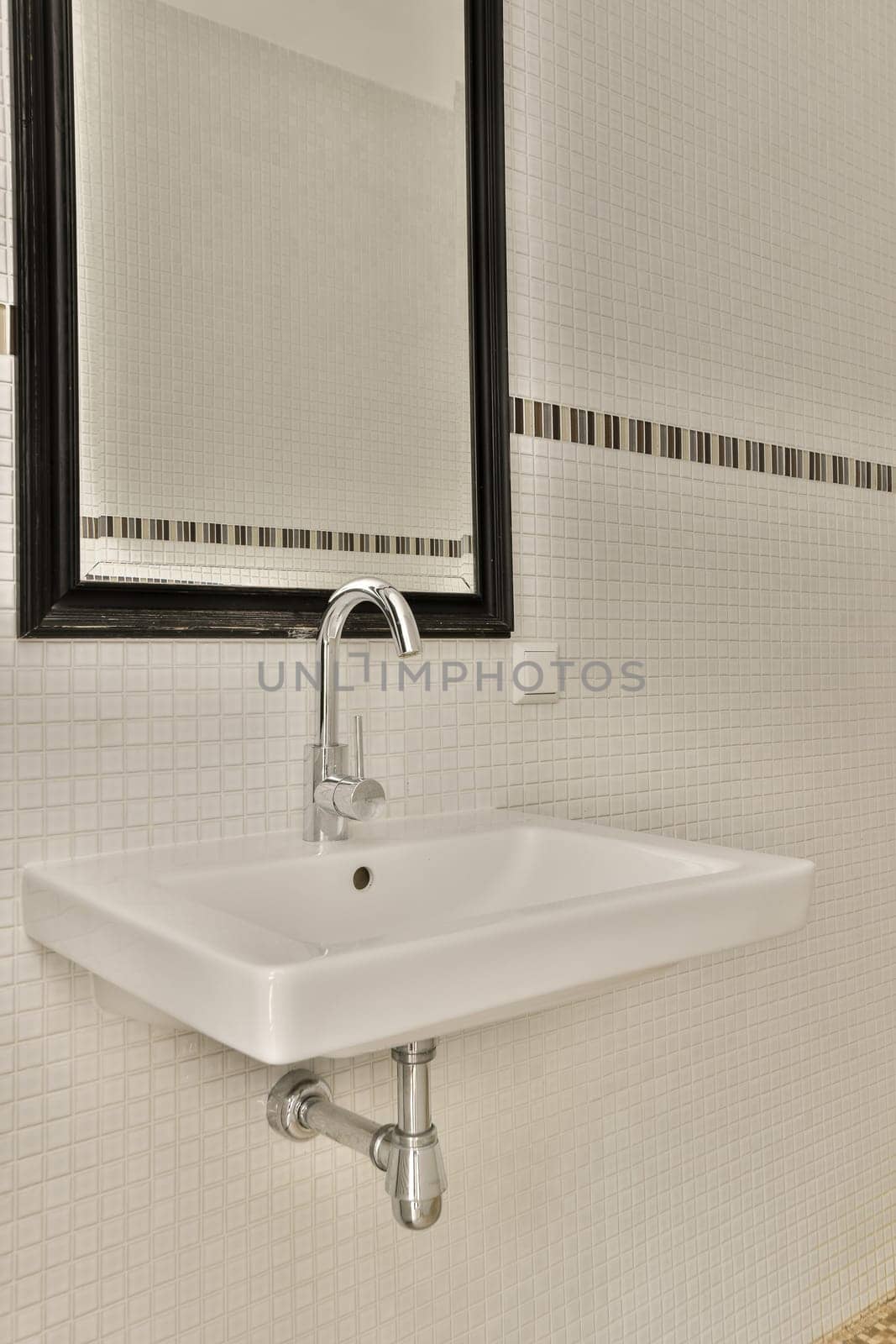 a bathroom with white tiles and black trim on the wall above the sink is a mirror that hangs over it