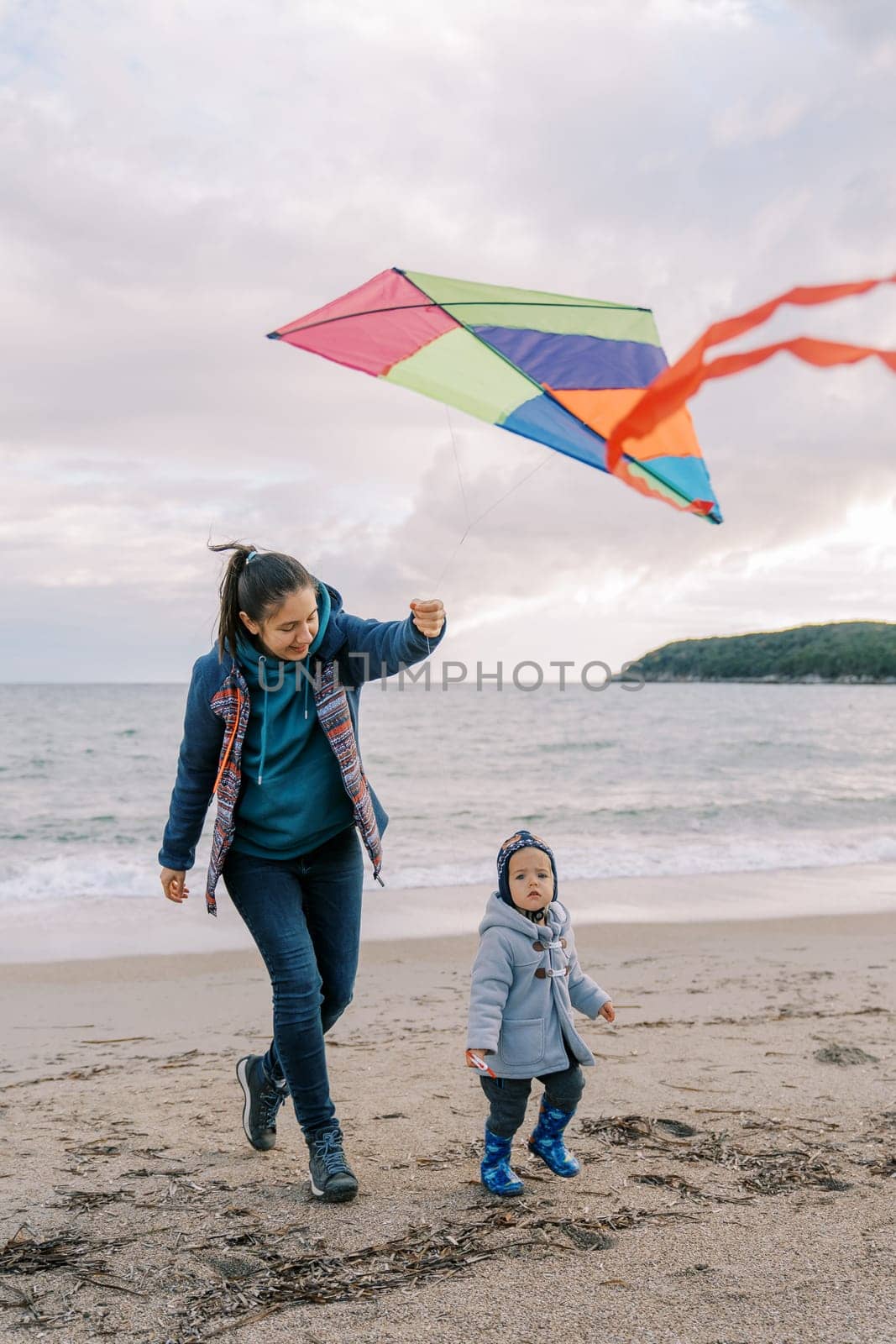 Little girl walks next to her mother with a colorful kite in her hand. High quality photo