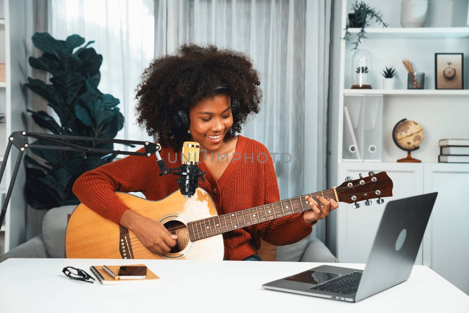 Host channel in musician of young African American playing guitar along with singing, broadcasting on laptop in studio. Decoration of equipment of headsets and recording microphone. Tastemaker.