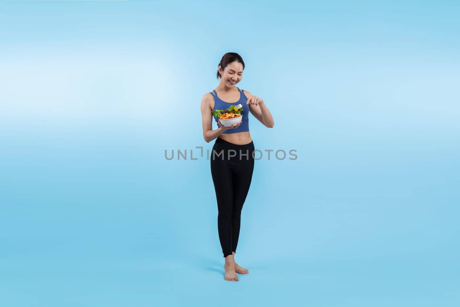 Asian woman in sportswear holding salad bowl on isolated background. Vigorous by biancoblue