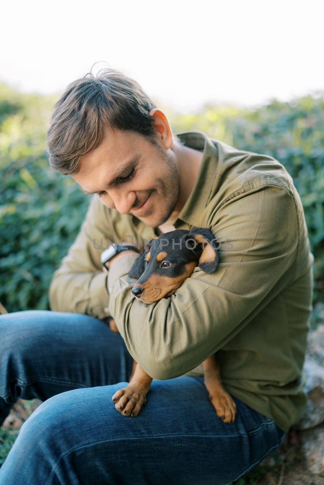 Young smiling man sitting with a puppy on his knees hugging and looking at him. High quality photo