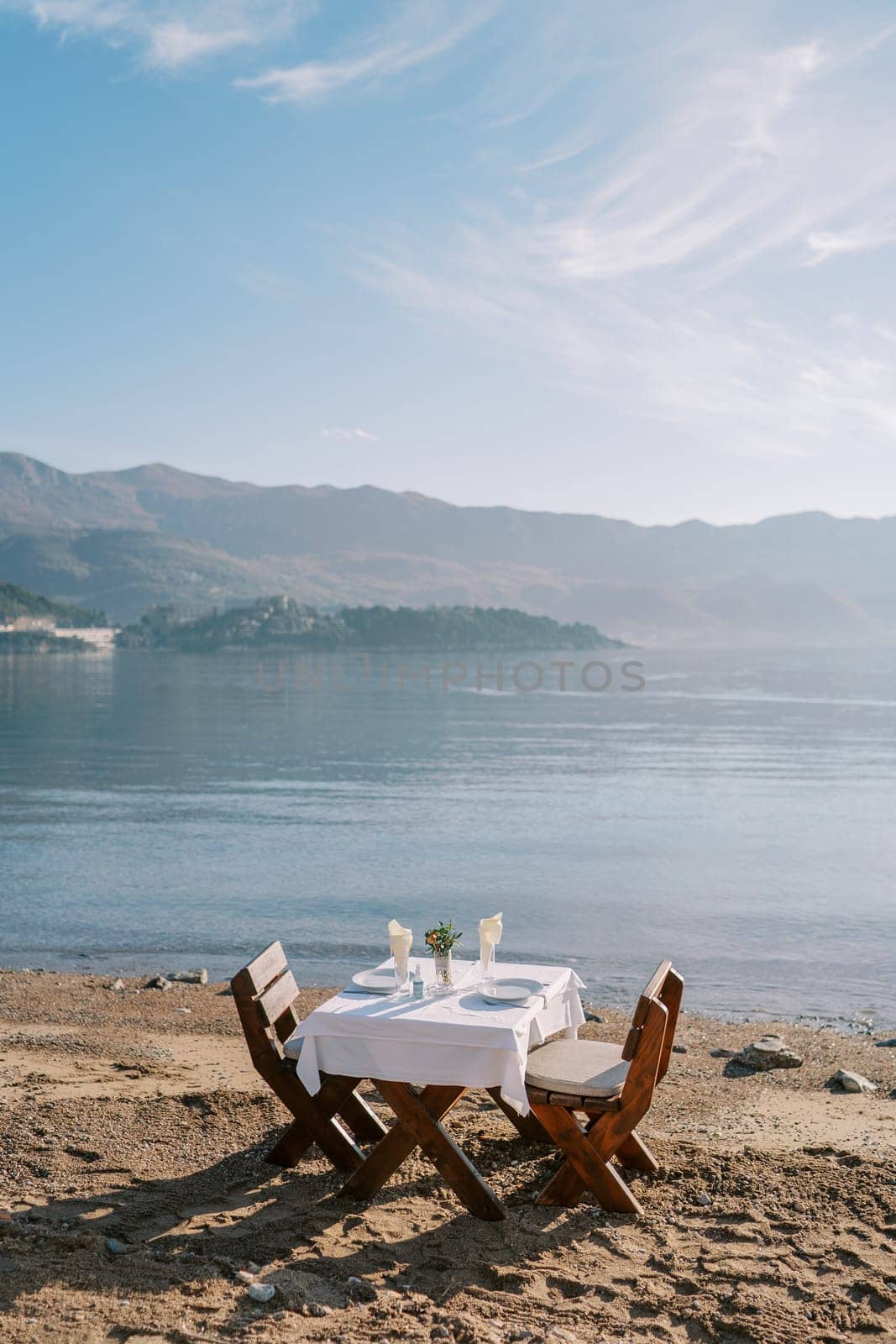 Laid table with chairs stands on a sandy beach by the sea with a view of the mountains. High quality photo