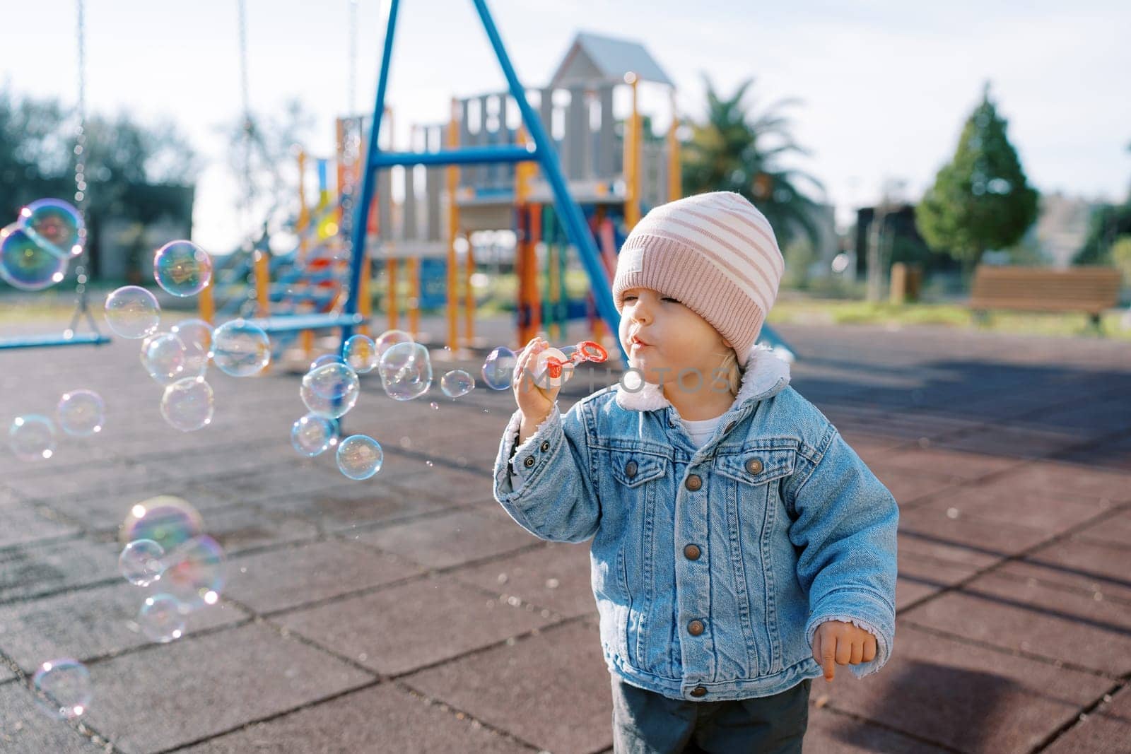 Little girl blowing soap bubbles on the playground. High quality photo