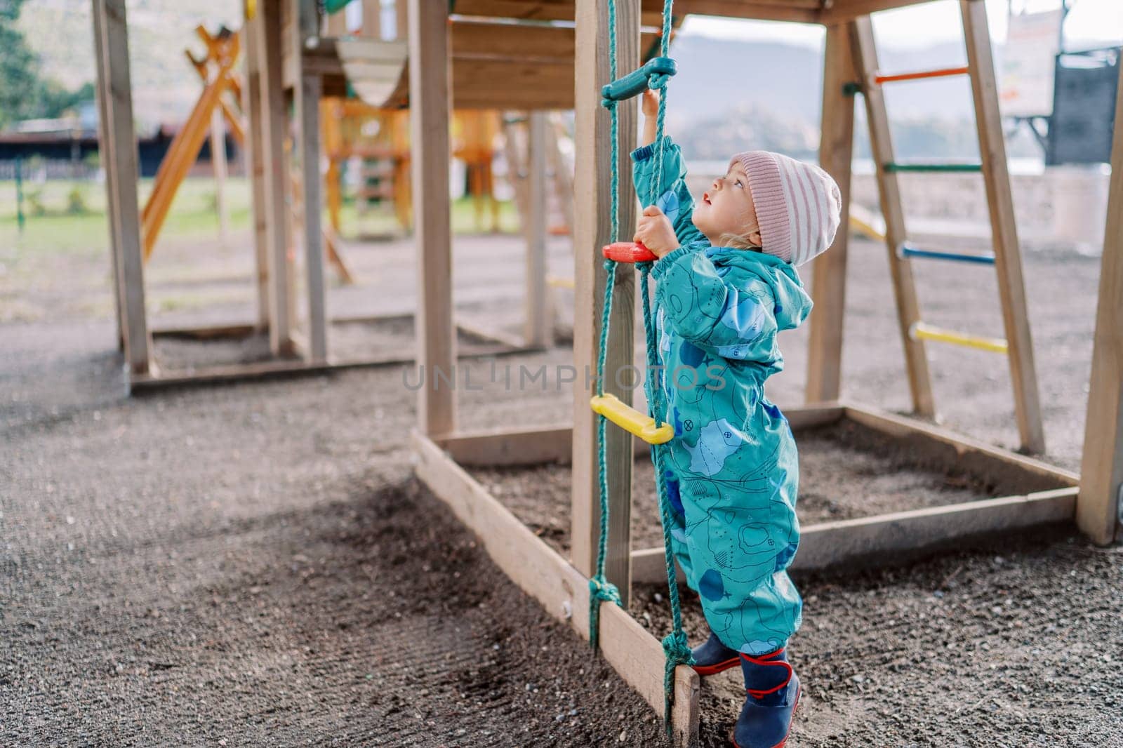 Little girl is trying to reach the top rung of a rope ladder by standing on her tiptoes. High quality photo